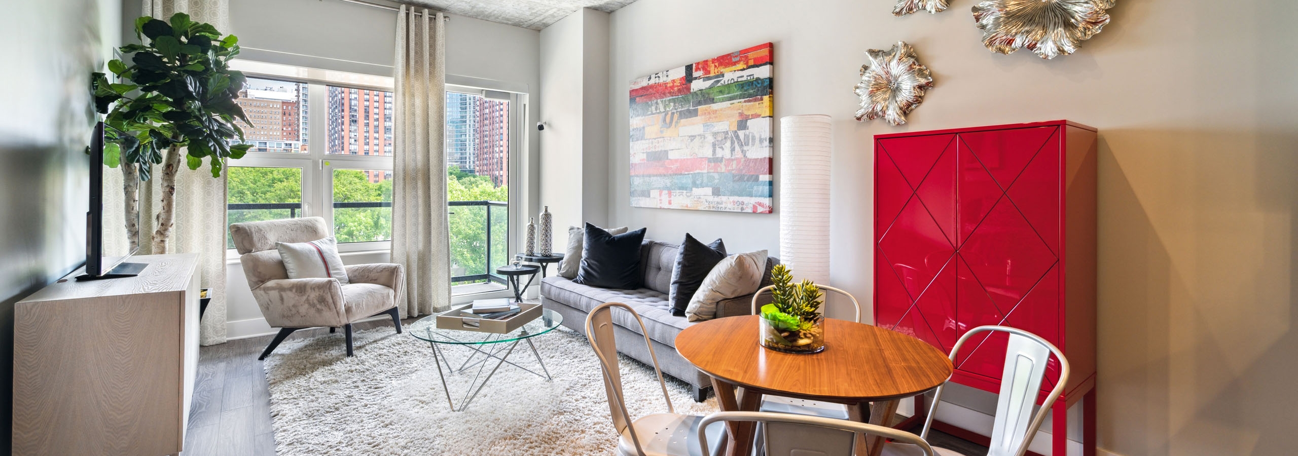 AMLI Lofts living and dining area featuring a small round dining table with metal chairs, plush furniture on a shag rug and a city view.