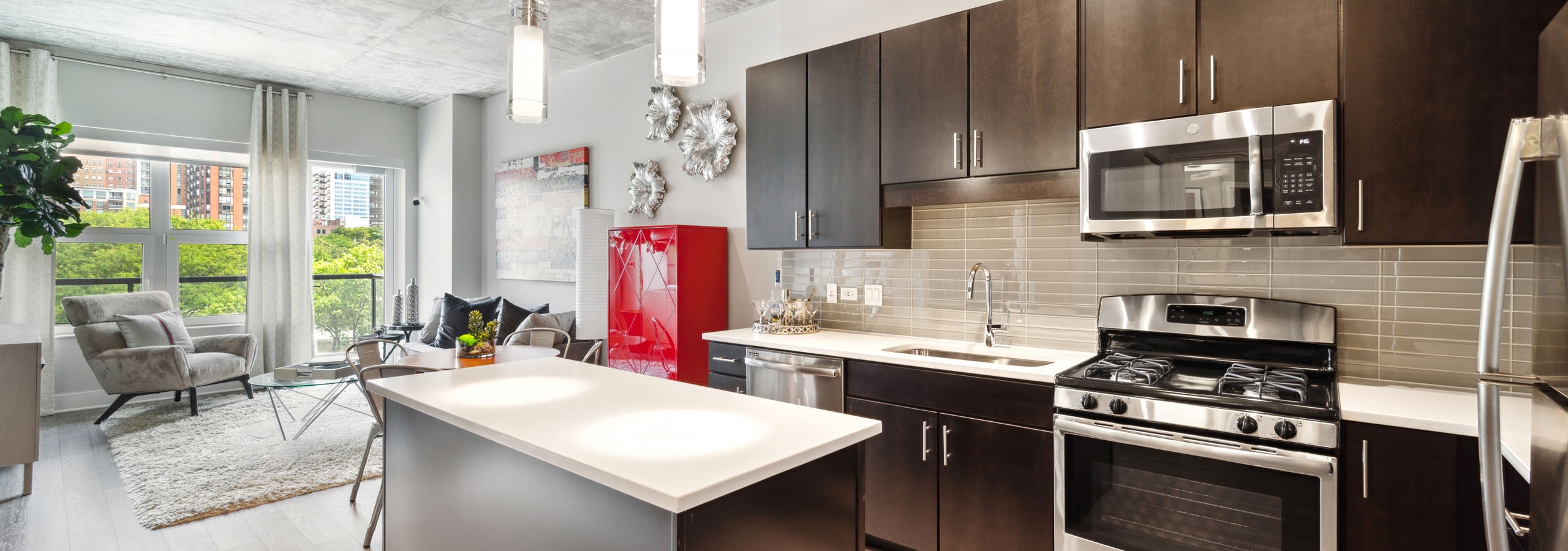 AMLI Lofts island kitchen with dark wood cabinetry, white quartz countertops, stainless steel appliances and a living area in the background.