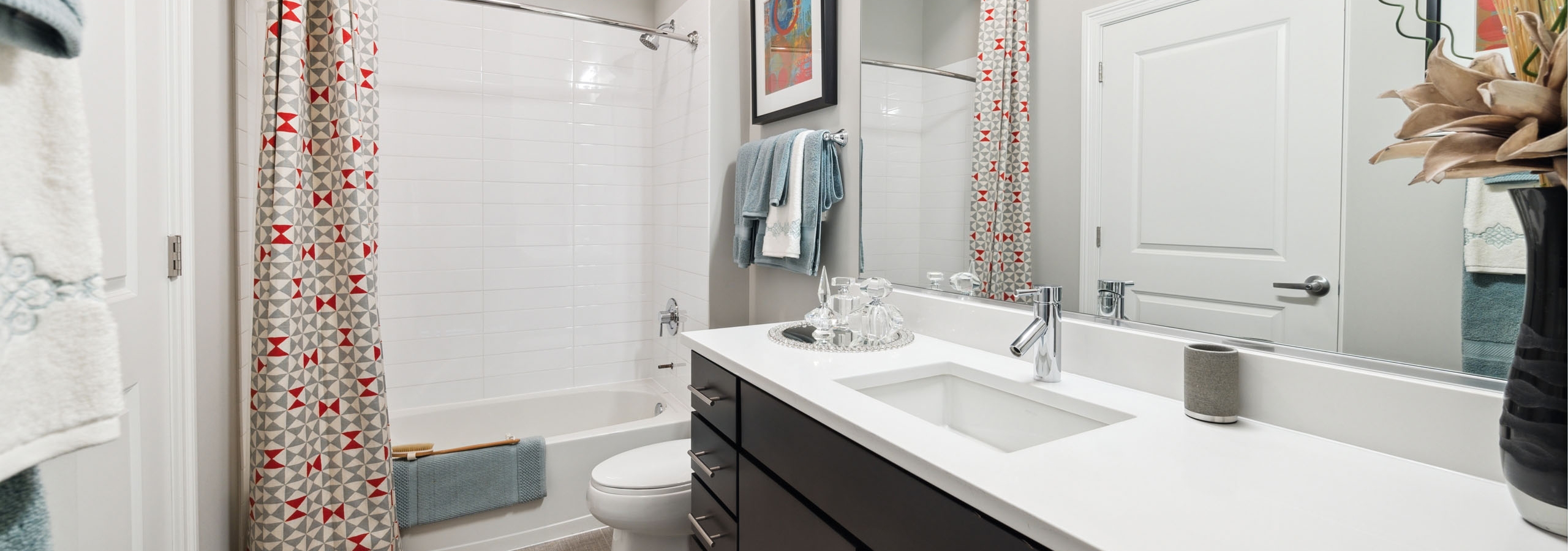 Bathroom with a white bathtub and a long white quartz counter atop a dark brown cabinet with a mirror above it at AMLI Lofts.