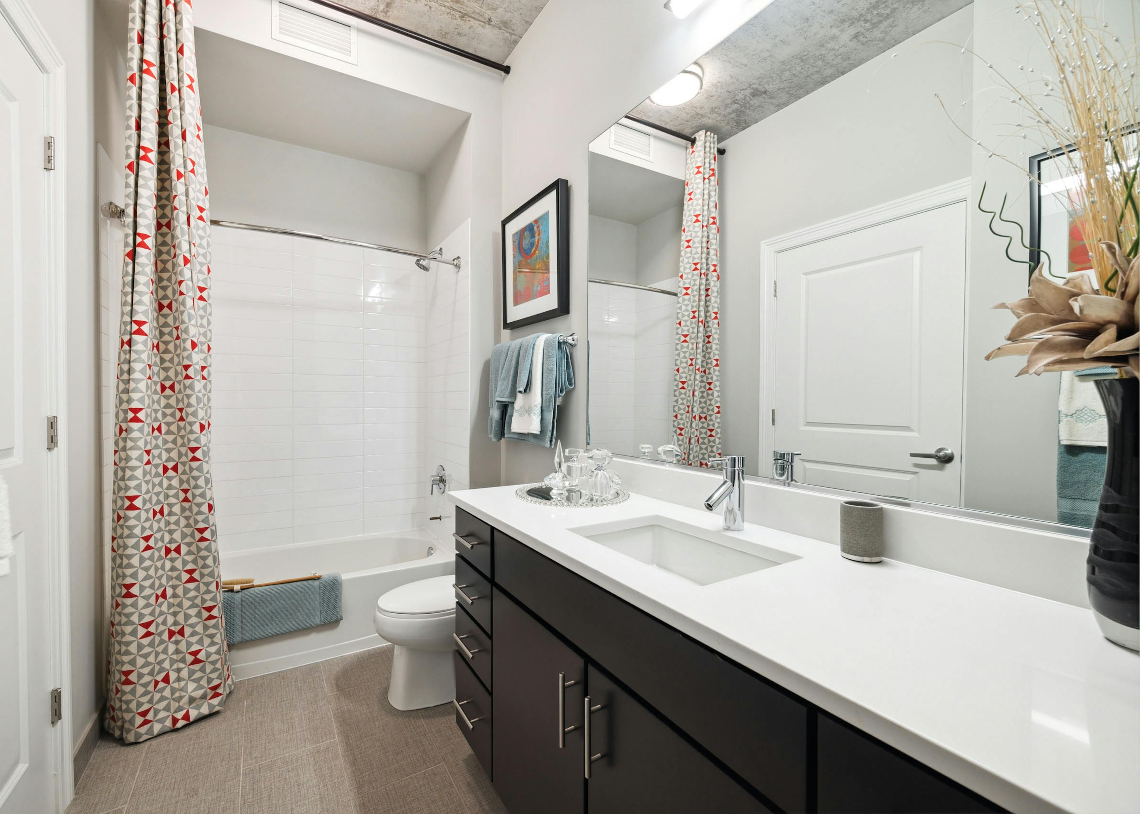 Bathroom with a white bathtub and a long white quartz counter atop a dark brown cabinet with a mirror above it at AMLI Lofts.