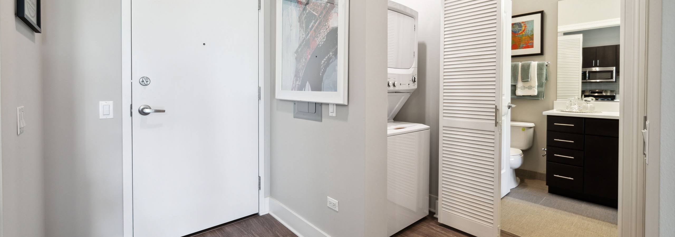 AMLI Lofts apartment featuring white front door, dark wood flooring and a stackable washer and dryer with a view into the bathroom.