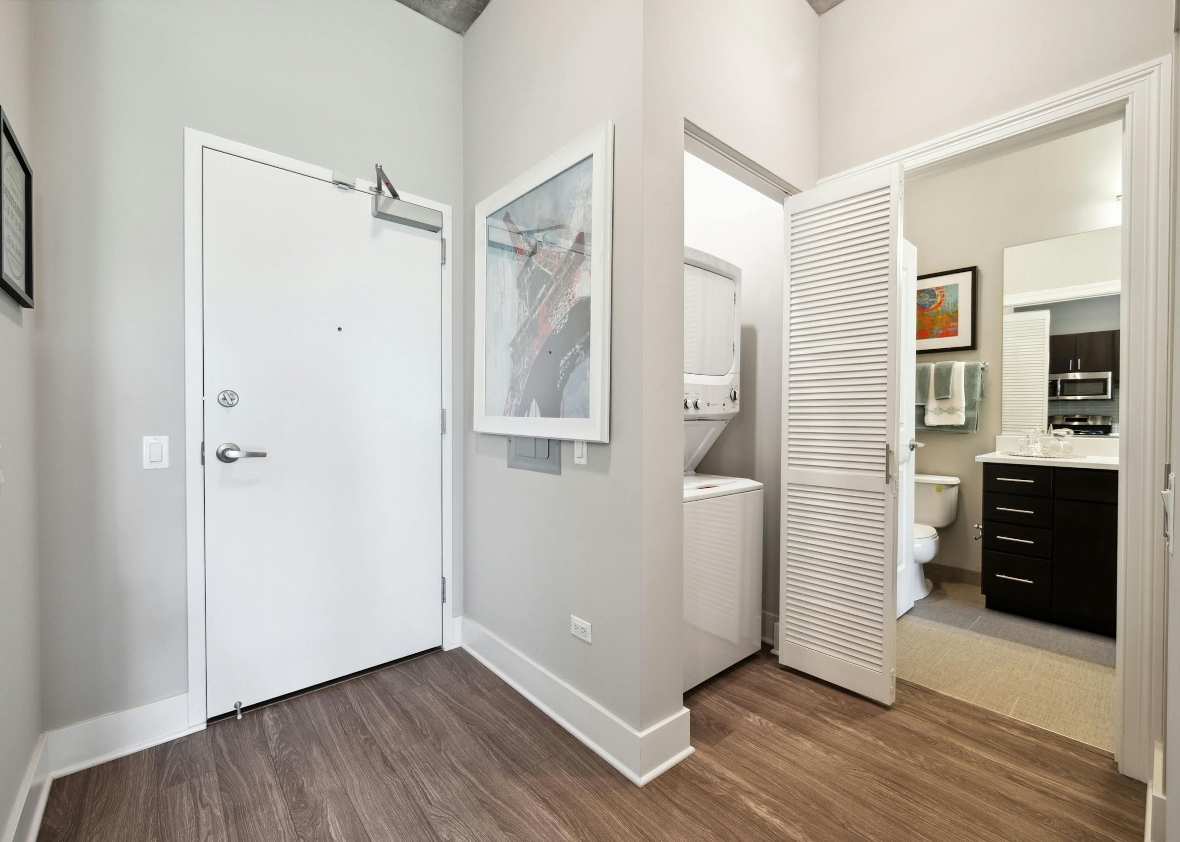 AMLI Lofts apartment featuring white front door, dark wood flooring and a stackable washer and dryer with a view into the bathroom.
