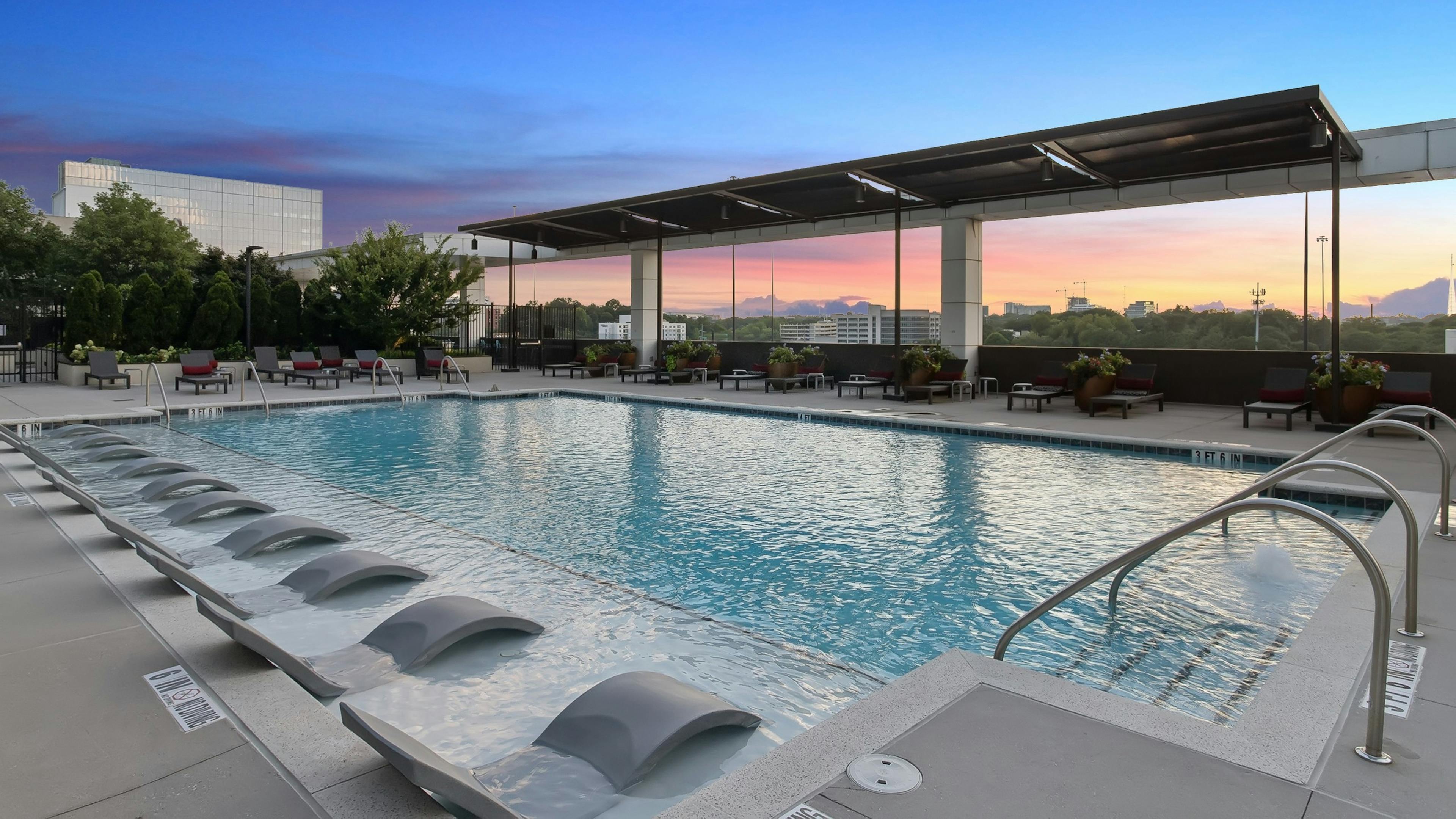 Sunset view of rooftop pool at AMLI Arts Center with lounge chairs partially submerged in water and surrounded by plants and patio furniture