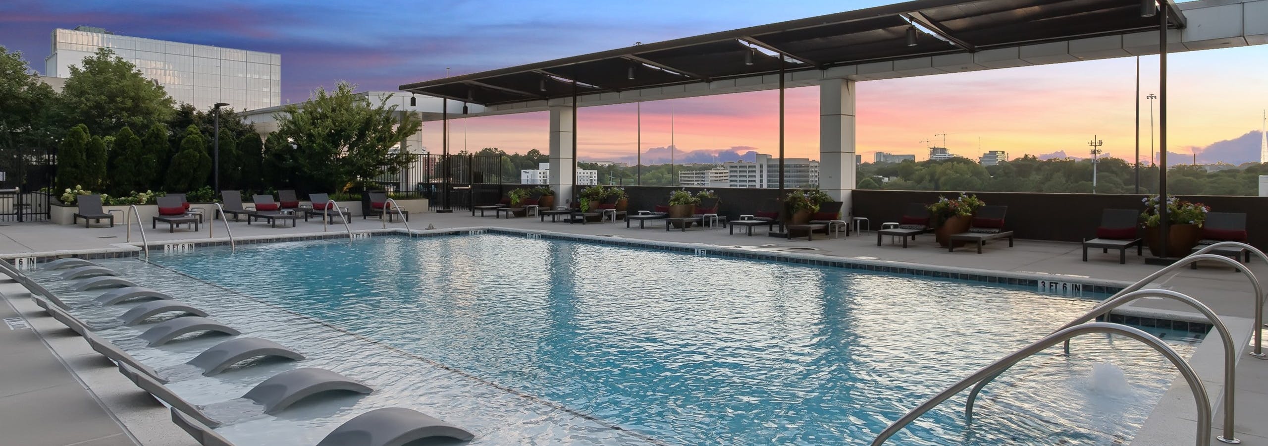 Sunset view of rooftop pool at AMLI Arts Center with lounge chairs partially submerged in water and surrounded by plants and patio furniture