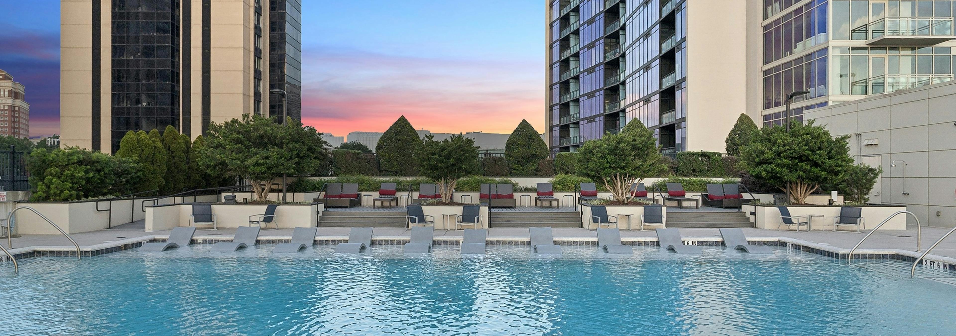 AMLI Arts Center rooftop pool surrounded by high-rise buildings and featuring several lounge chairs under a sunset sky