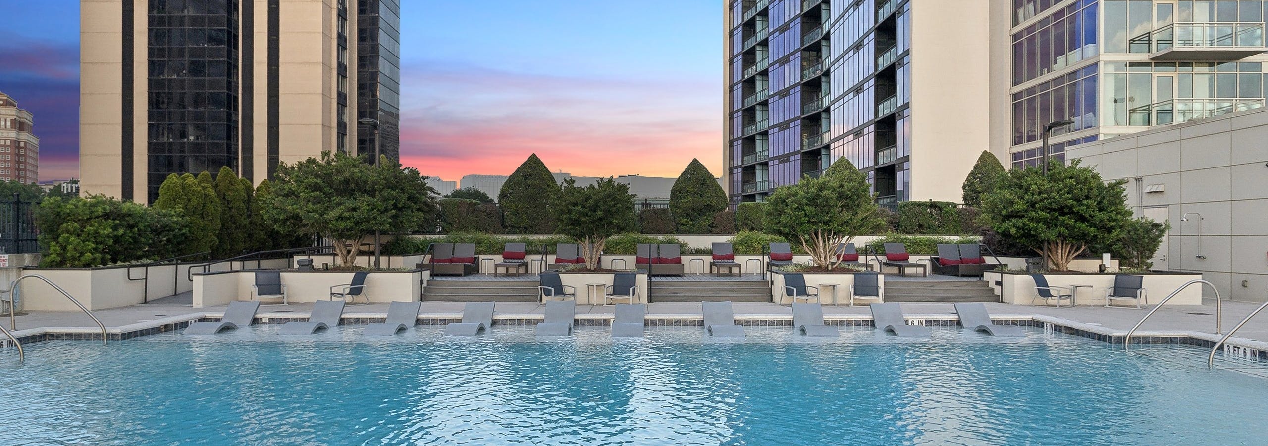 AMLI Arts Center rooftop pool surrounded by high-rise buildings and featuring several lounge chairs under a sunset sky
