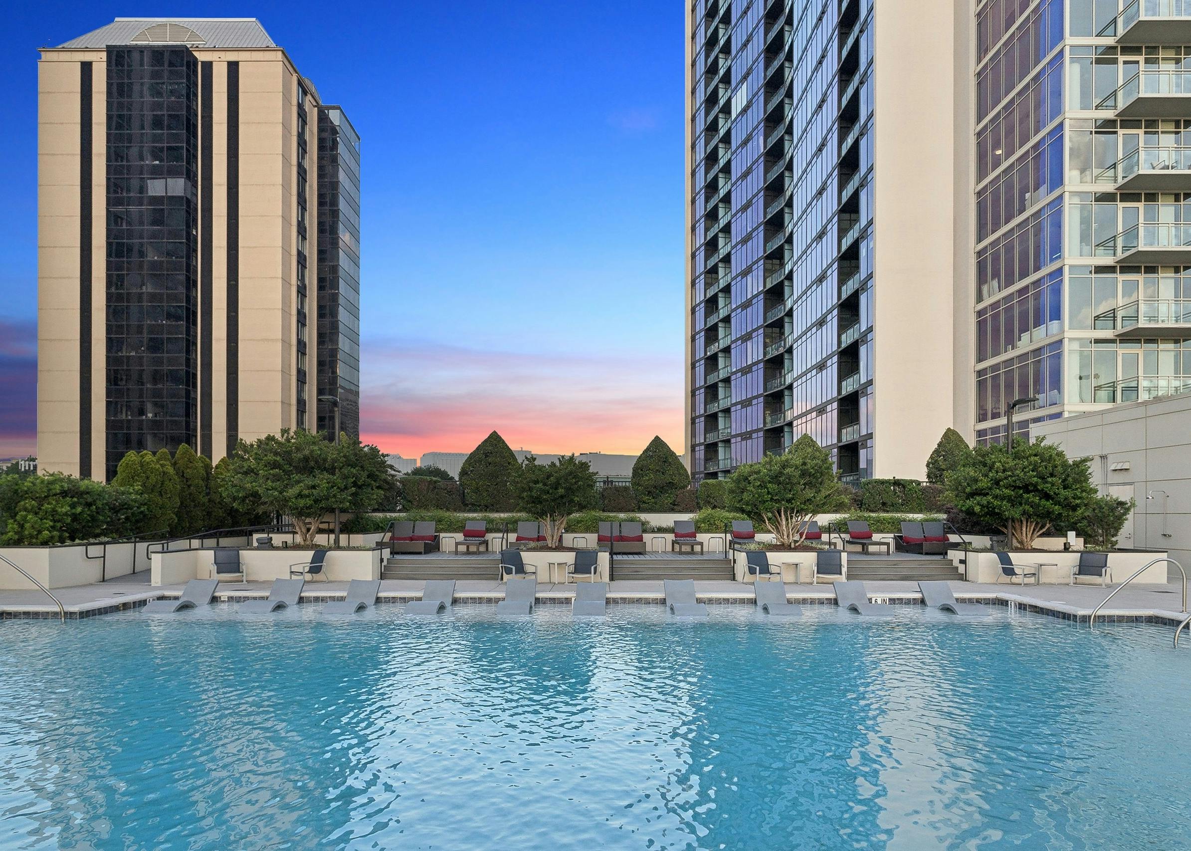 AMLI Arts Center rooftop pool surrounded by high-rise buildings and featuring several lounge chairs under a sunset sky