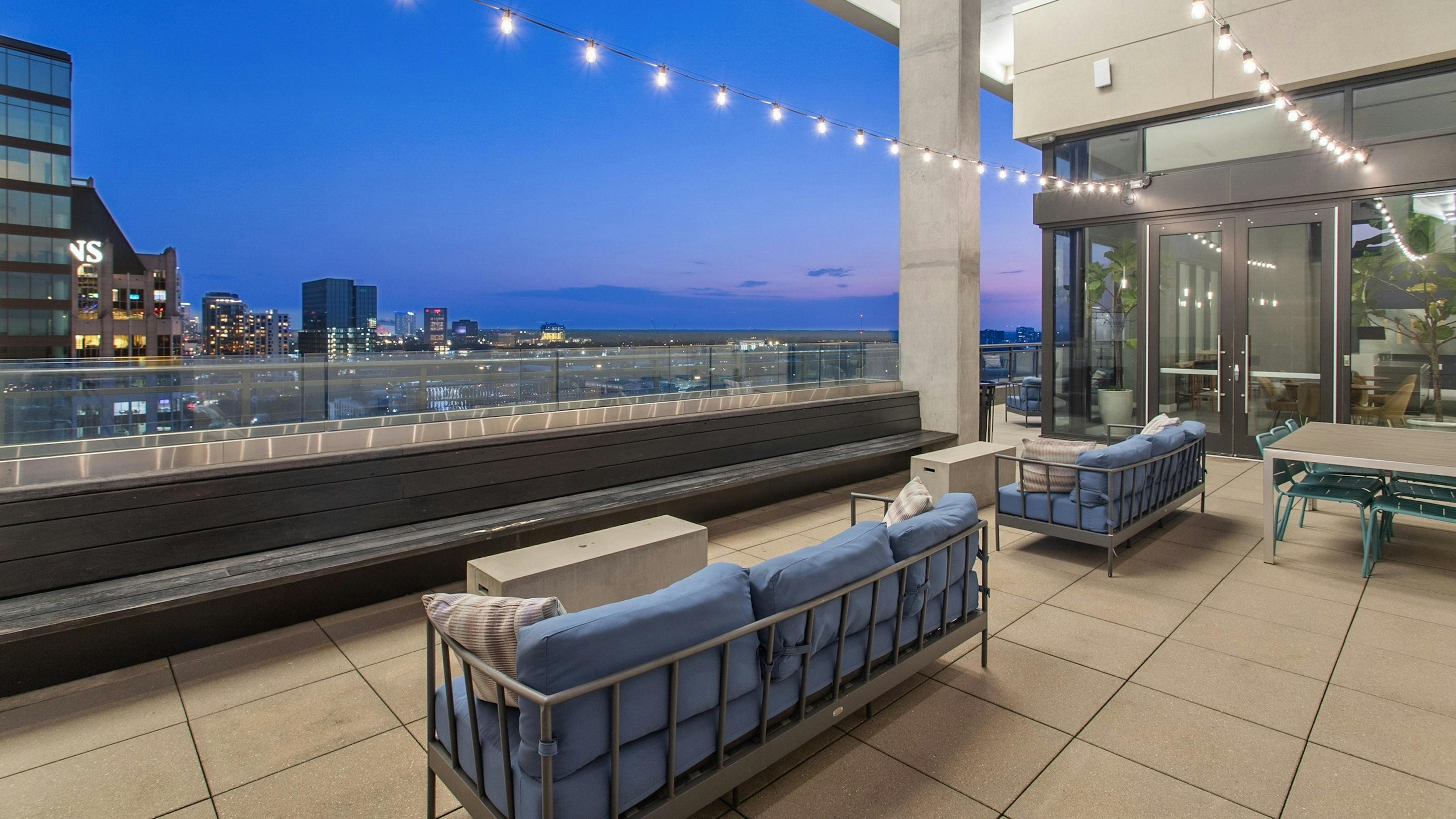 Nighttime view from AMLI Arts Center rooftop with blue outdoor couches overlooking the city with string lights hanging above