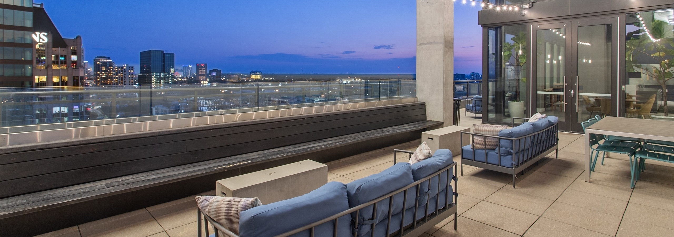 Nighttime view from AMLI Arts Center rooftop with blue outdoor couches overlooking the city with string lights hanging above