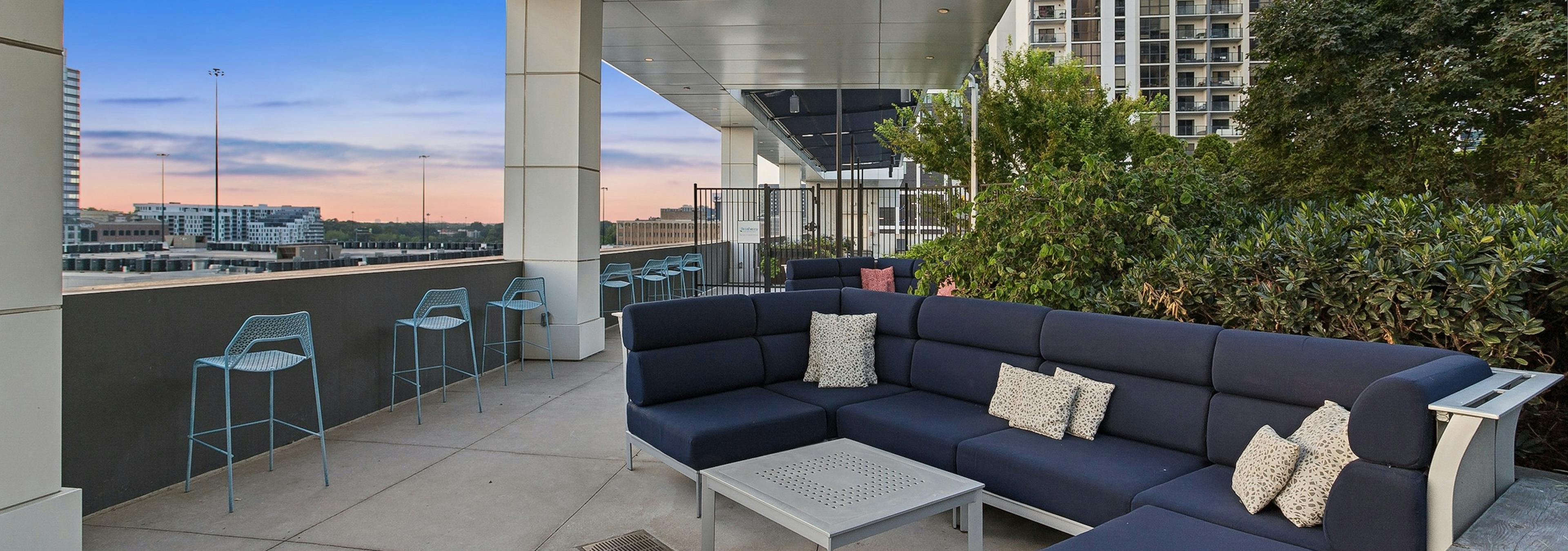 Sunset view of outdoor rooftop terrace at AMLI Arts Center with a large navy L shaped sofa with navy cushions and silver coffee table