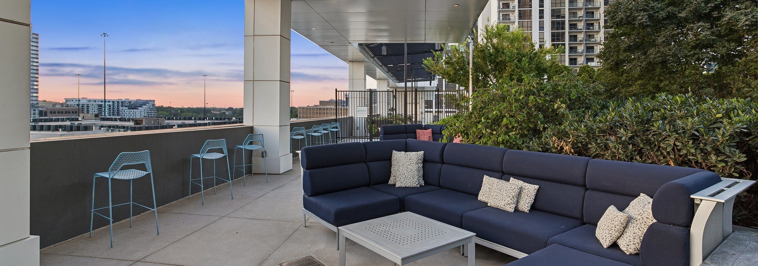Sunset view of outdoor rooftop terrace at AMLI Arts Center with a large navy L shaped sofa with navy cushions and silver coffee table