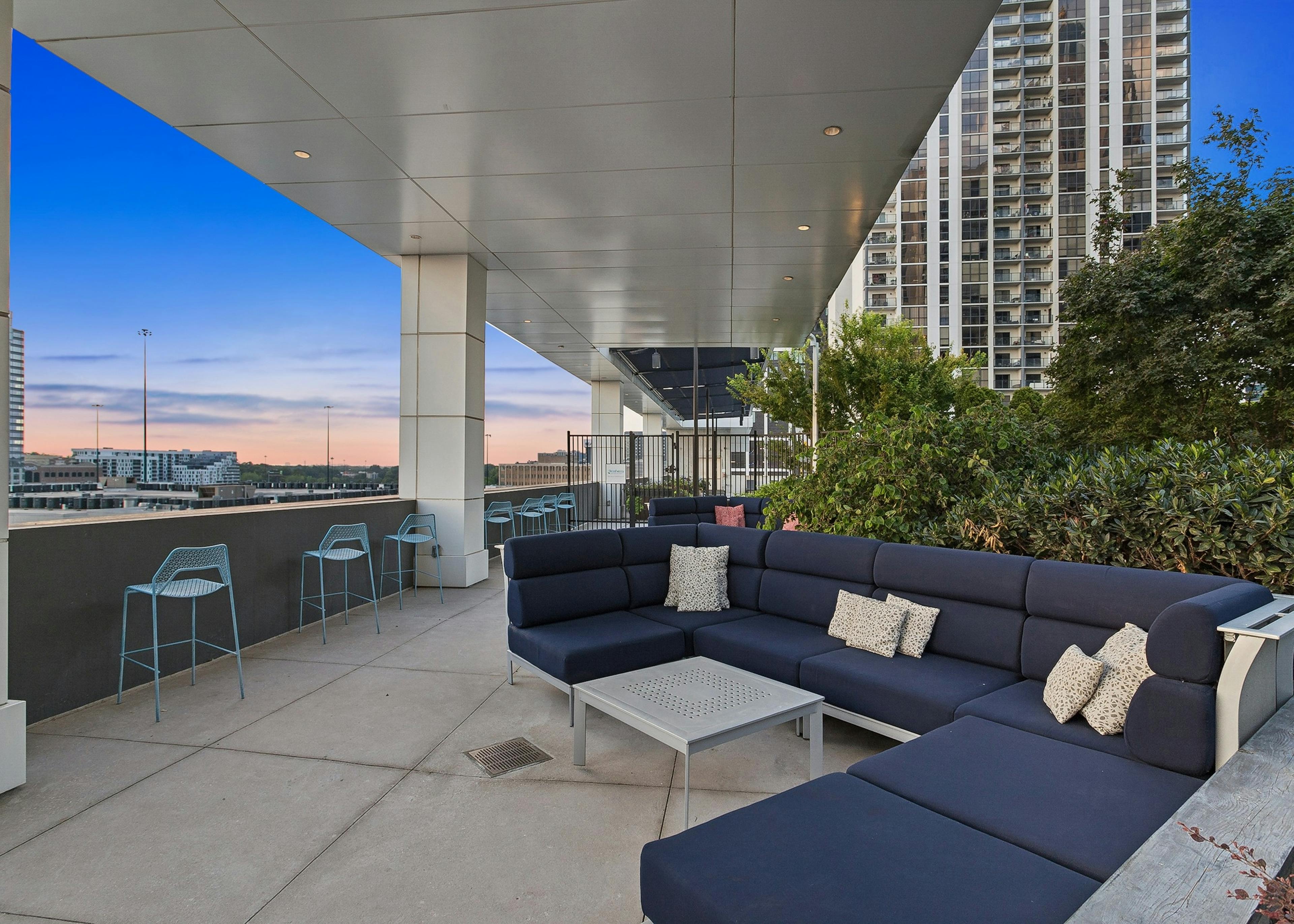 Sunset view of outdoor rooftop terrace at AMLI Arts Center with a large navy L shaped sofa with navy cushions and silver coffee table