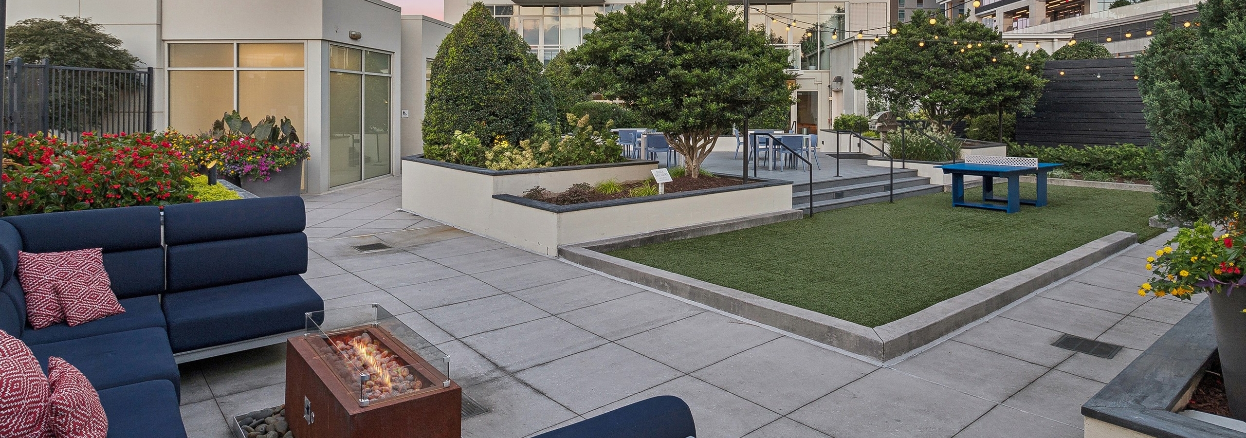 AMLI Arts Center rooftop patio with a fire pit and navy couch  and turf area with ping pong table surrounded by trees and flowers