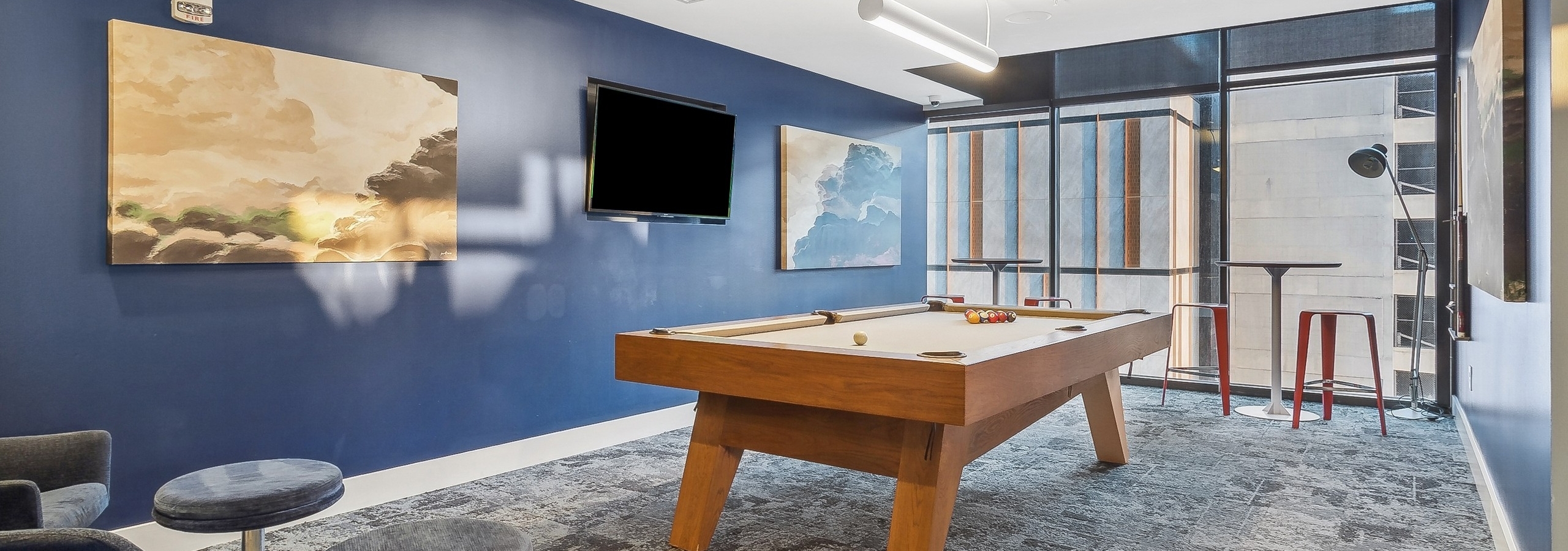 Game room at AMLI Arts Center with a pool table in the center with and abstract paintings and a wall mounted television on a blue wall