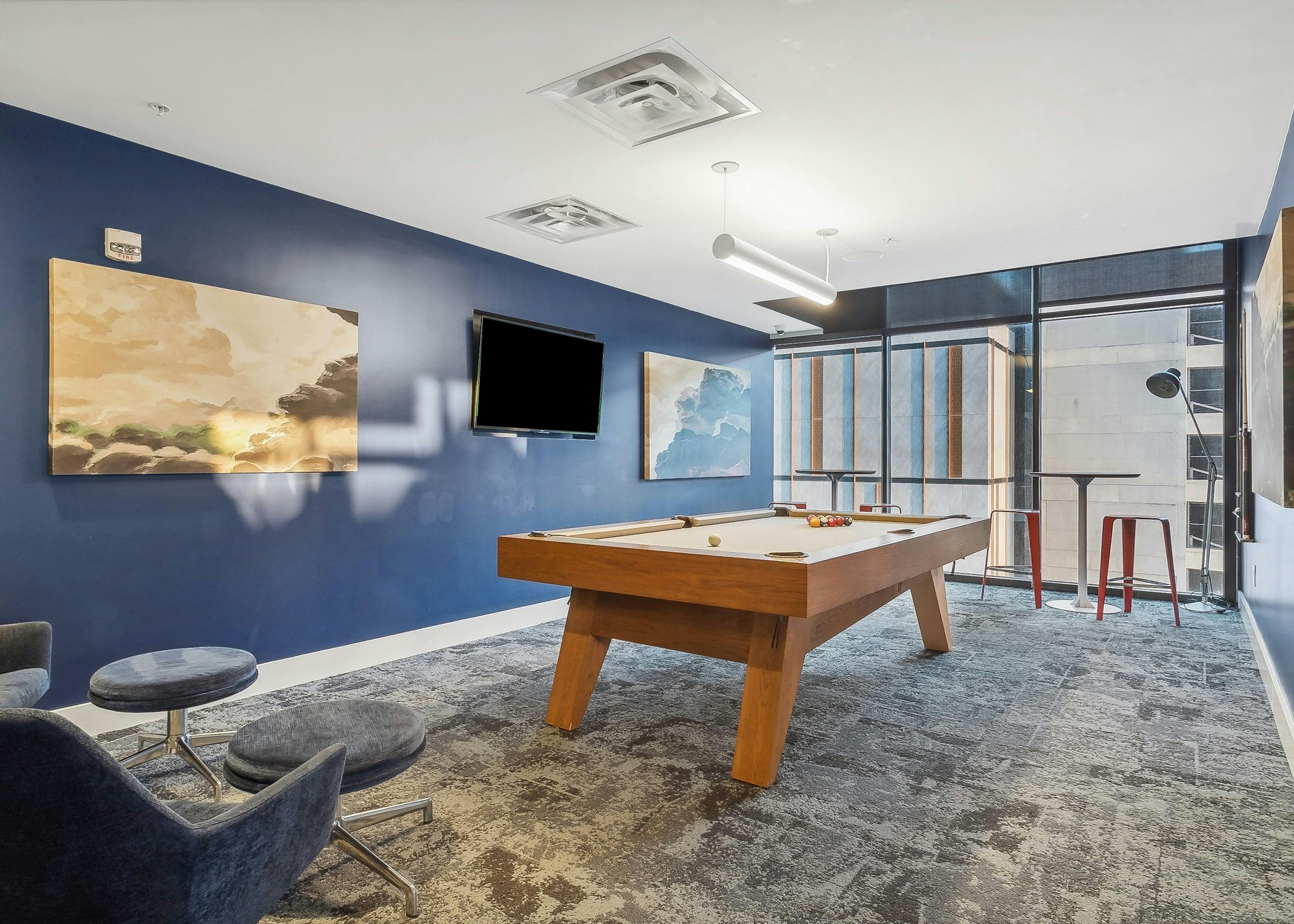 Game room at AMLI Arts Center with a pool table in the center with and abstract paintings and a wall mounted television on a blue wall