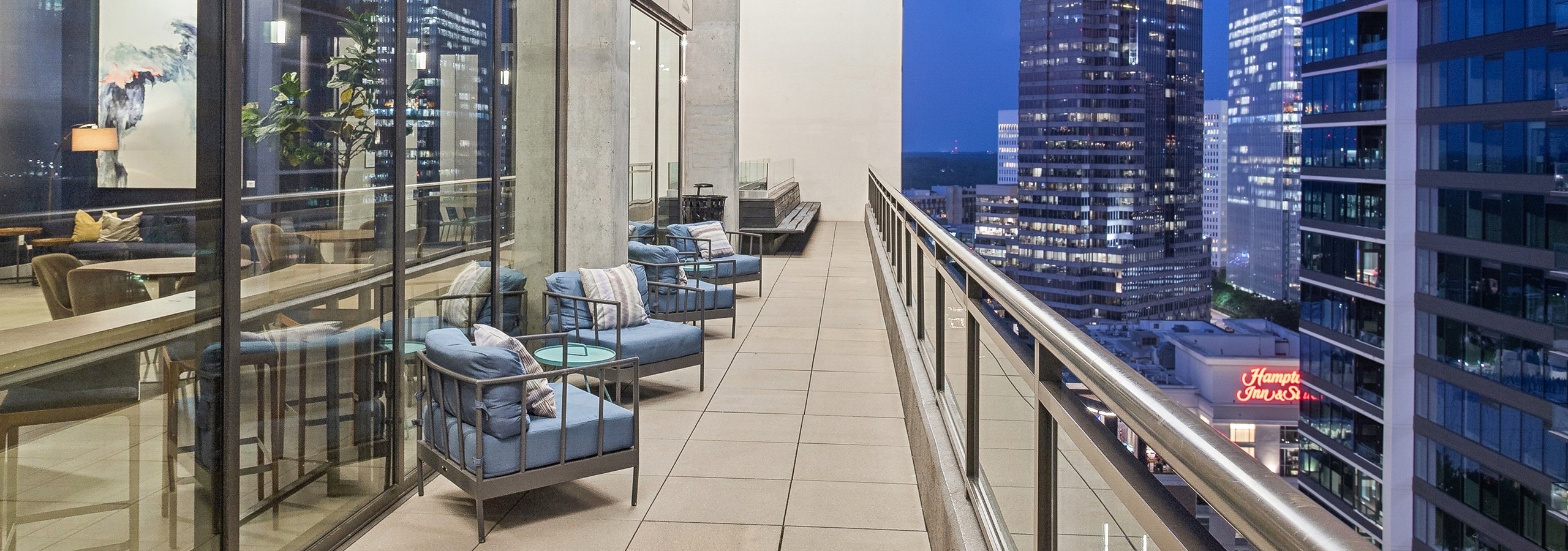 Skydeck balcony area at AMLI Arts Center with glass and stainless railing and blue padded chairs overlooking cityscape at night