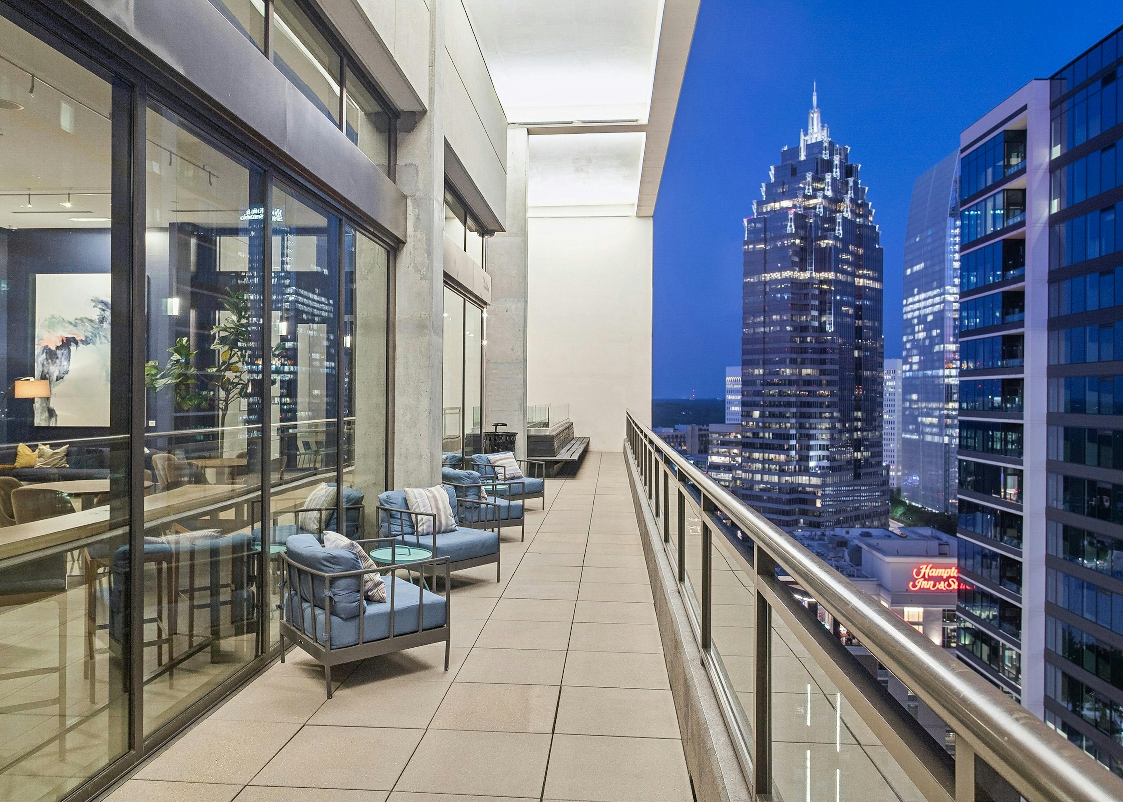 Skydeck balcony area at AMLI Arts Center with glass and stainless railing and blue padded chairs overlooking cityscape at dusk