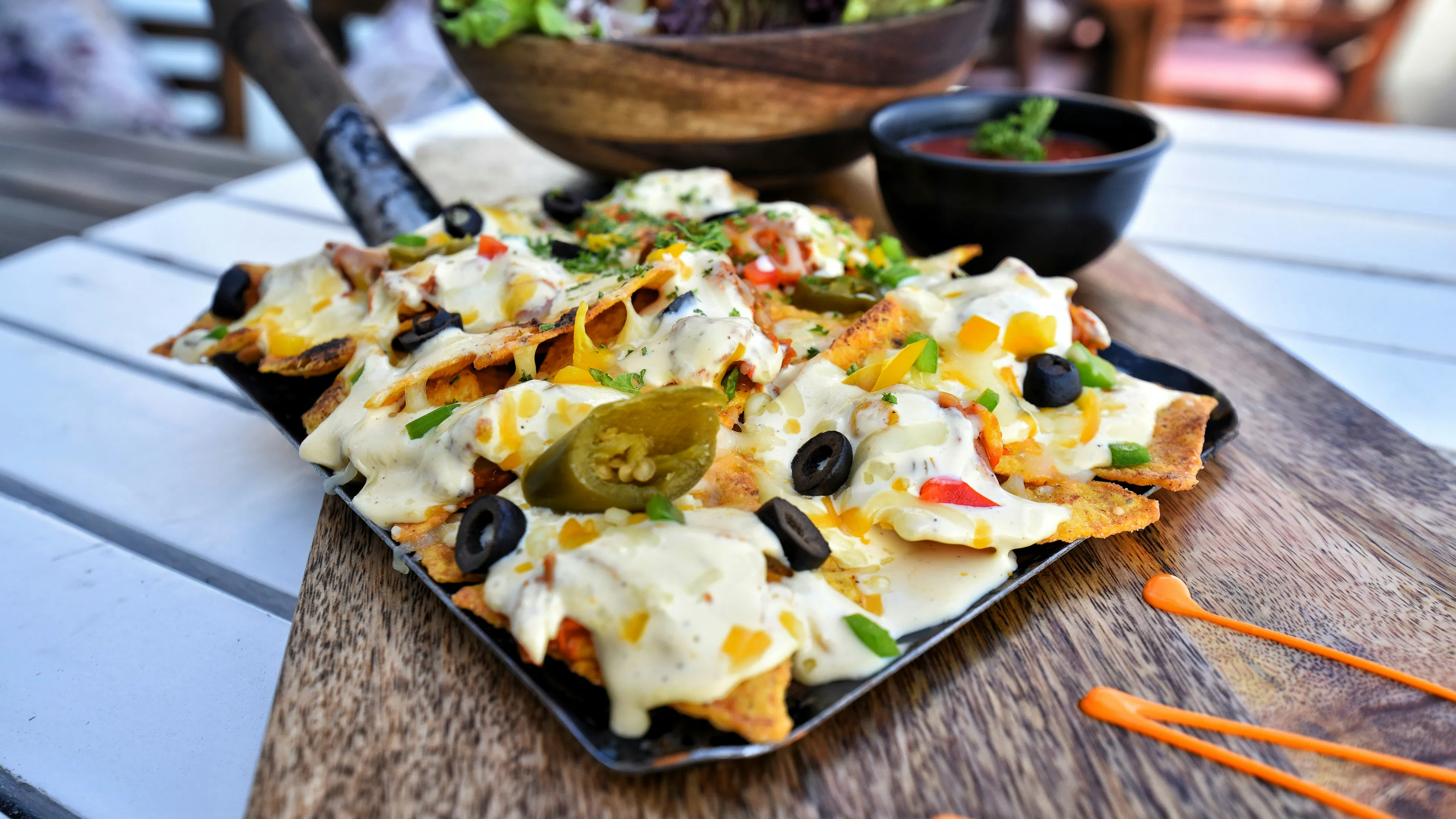 A plate of nachos piled high with white queso and jalapenos on a wooden cutting board