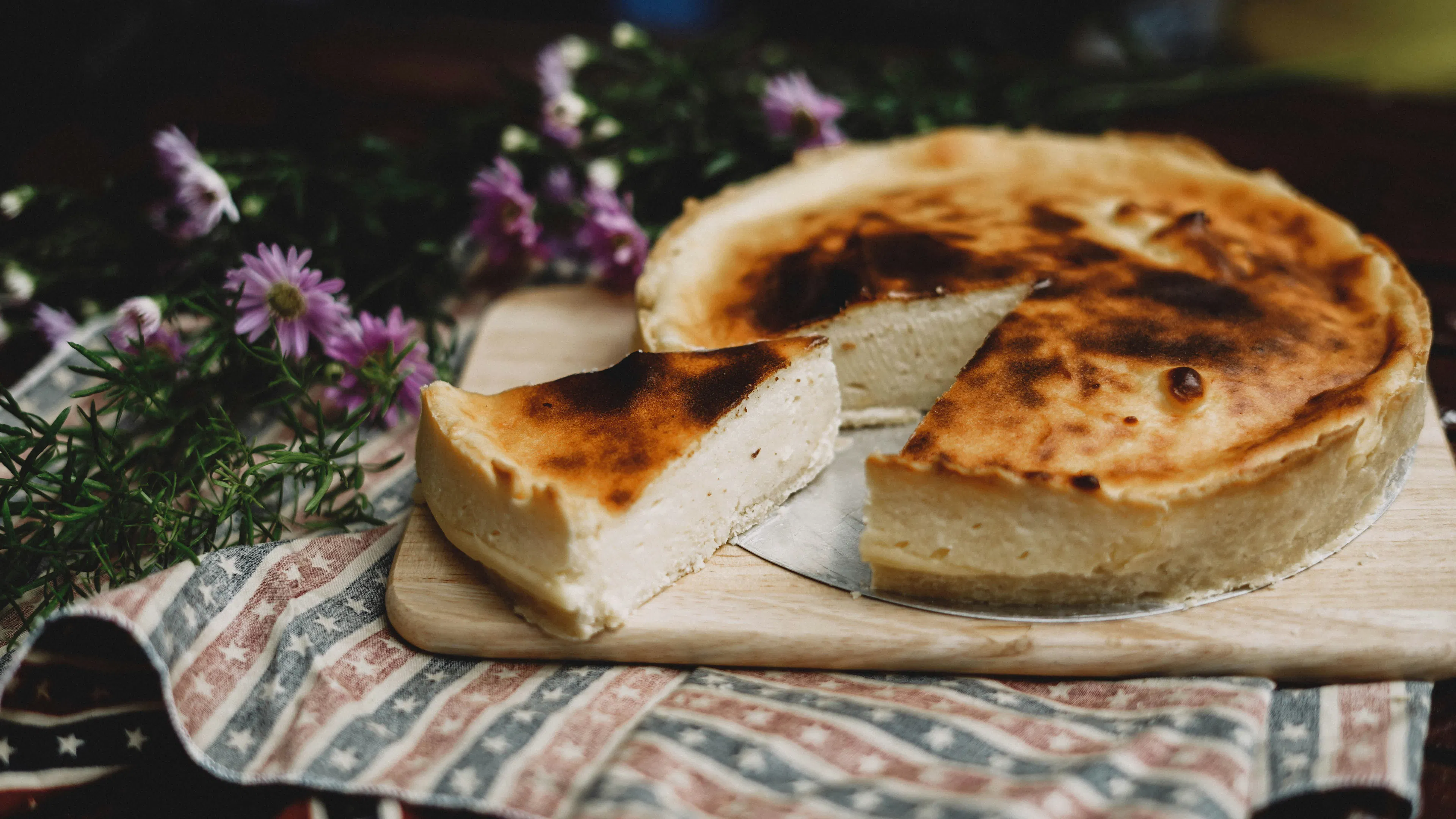 A basque burnt cheesecake with a slice cut out of it on a wooden cutting board