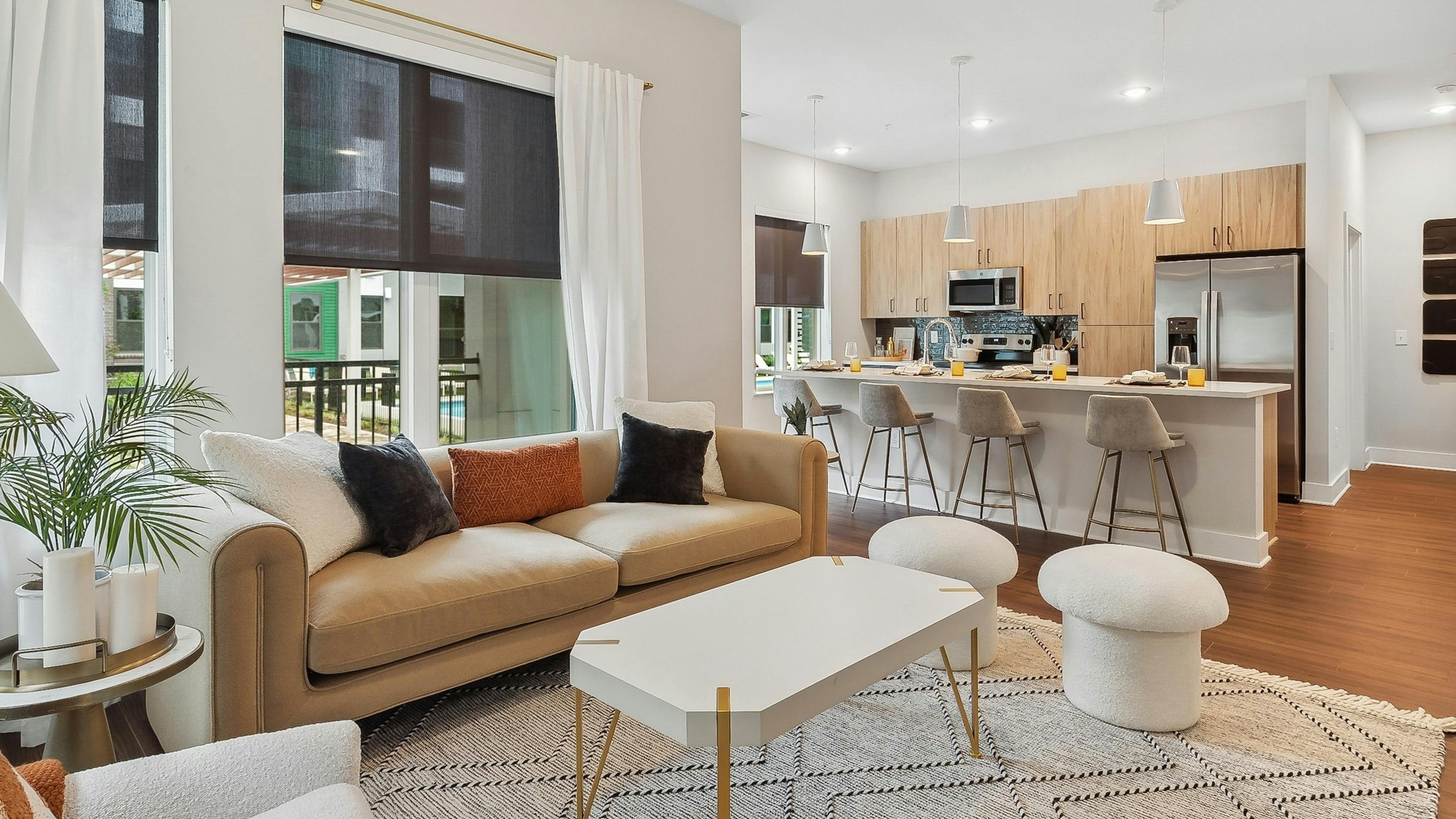 AMLI Flatiron living room with a beige sofa with orange and black pillows and a white coffee table with view of kitchen in rear