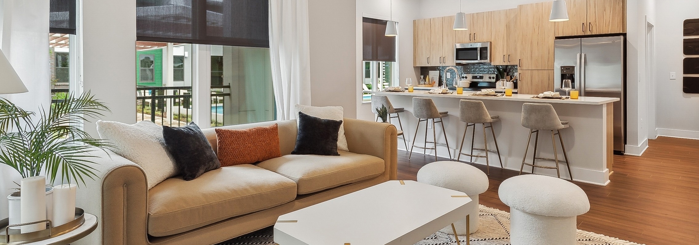AMLI Flatiron living room with a beige sofa with orange and black pillows and a white coffee table with view of kitchen in rear
