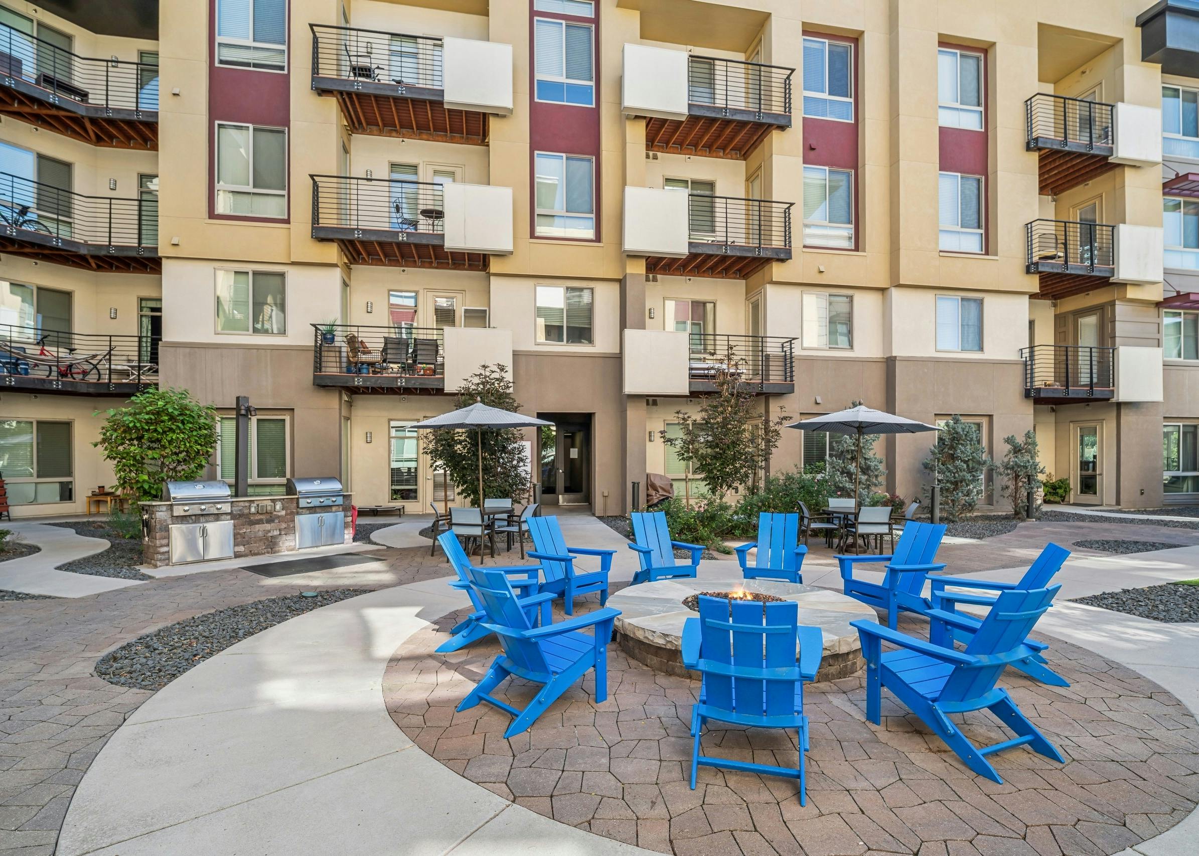 Courtyard fire pit at AMLI Cherry Creek apartments surrounded by blue Adirondack chairs and with grill, tables and chairs in the rear