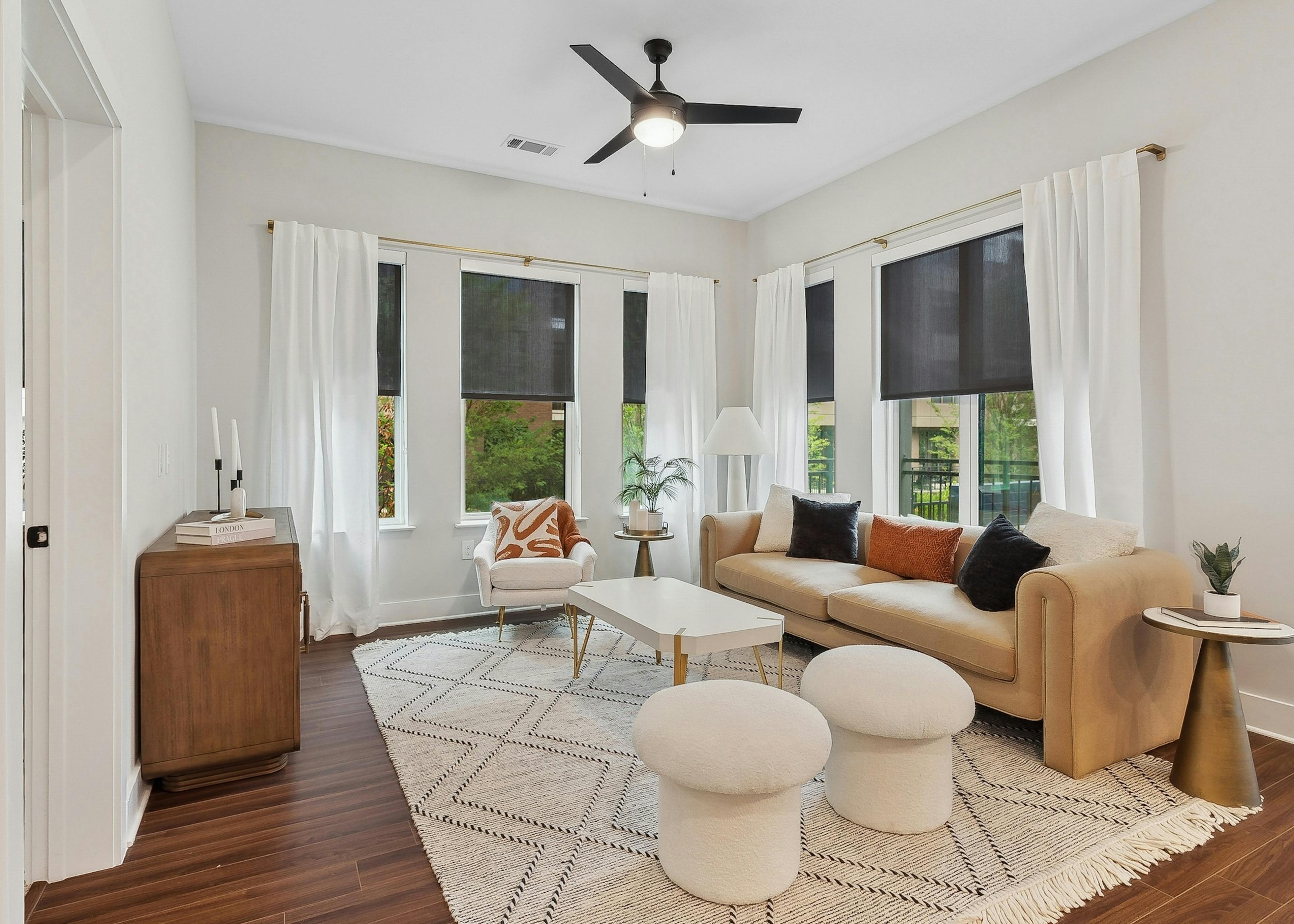 Living room at AMLI Flatiron featuring a tan sofa and white armchair around a white coffee table and white curtains and black roller shades