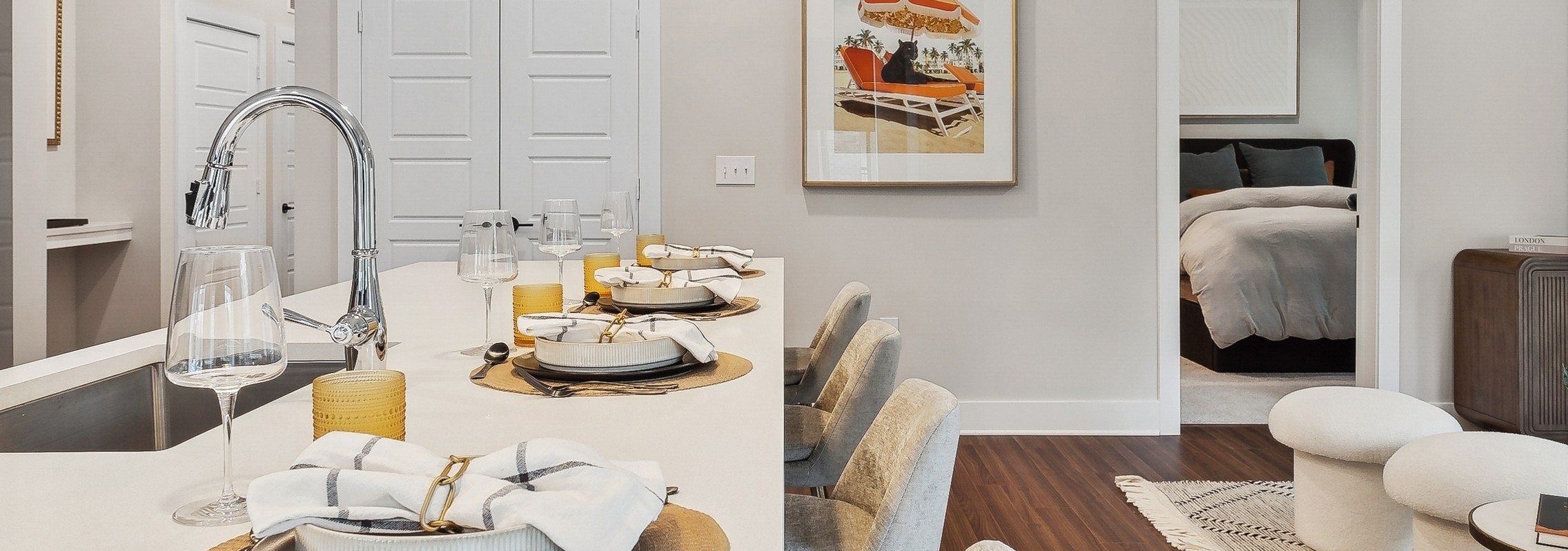 Kitchen at AMLI Flatiron with large white island with table settings and a view into a bedroom with a framed picture of an orange umbrella
