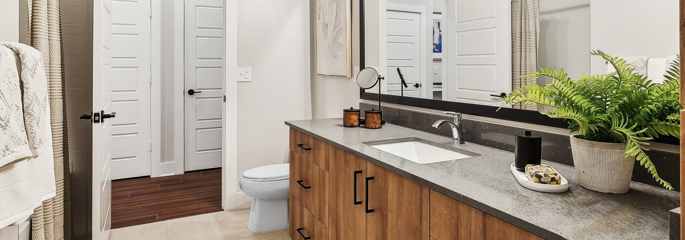 AMLI Flatiron apartment bathroom with a large mirror above a long wooden vanity with a stone countertop and white sink