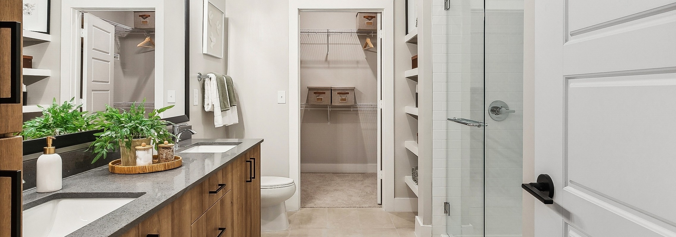 Modern bathroom at AMLI Flatiron featuring a double wooden vanity with a large mirror above and glass shower with view into walk-in closet