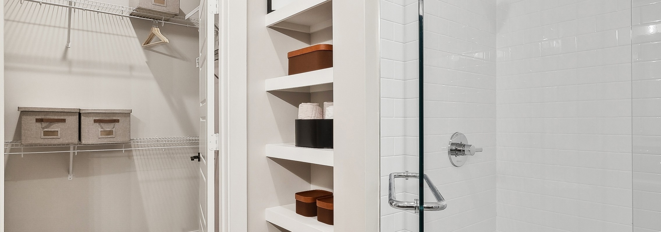AMLI Flatiron bathroom featuring a shower with white tile walls and a view into a closet with shelves holding organized bins and towels