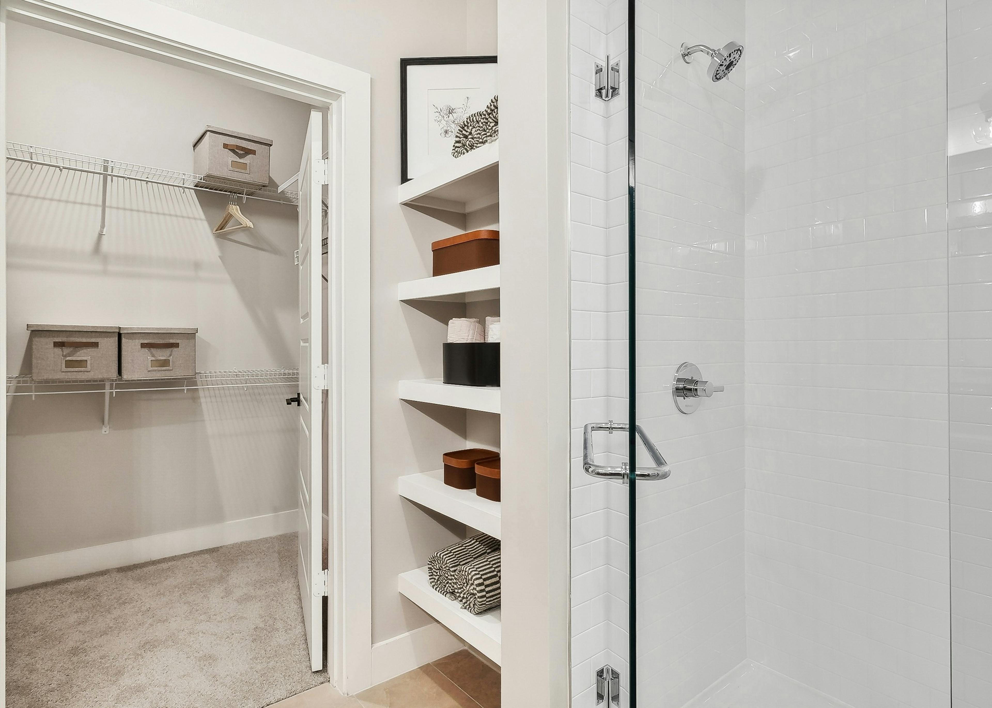 AMLI Flatiron bathroom featuring a shower with white tile walls and a view into a closet with shelves holding organized bins and towels