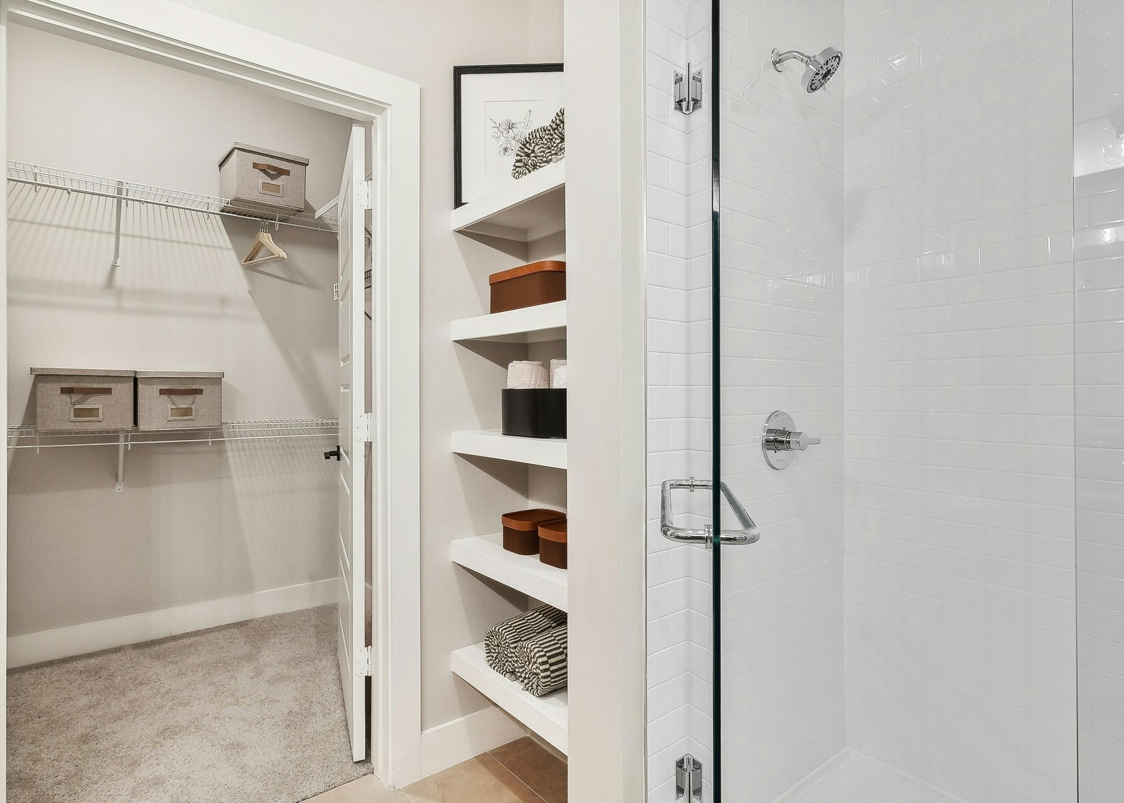 AMLI Flatiron bathroom featuring a shower with white tile walls and a view into a closet with shelves holding organized bins and towels