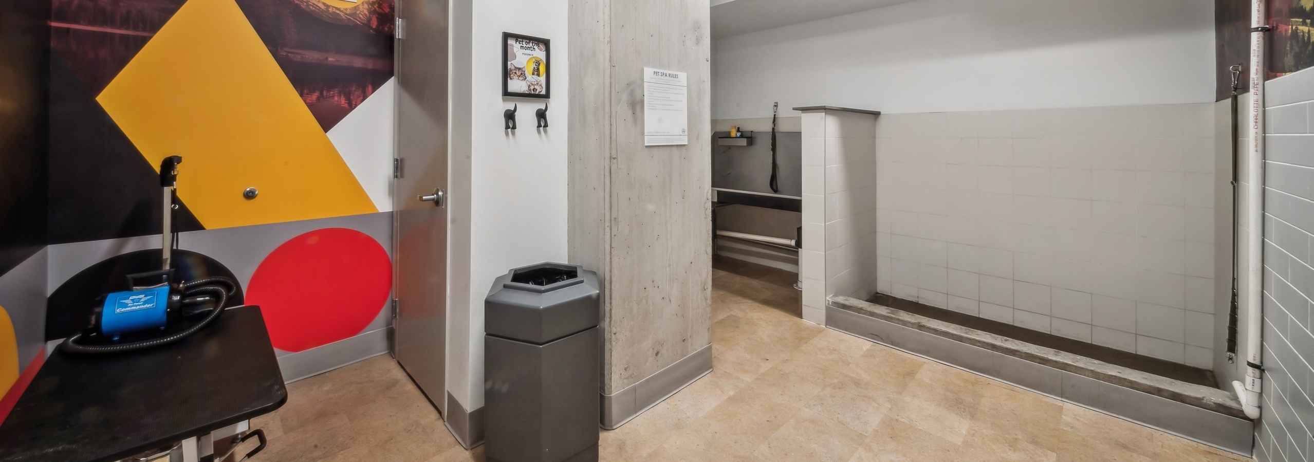 A paw wash at AMLI Broadway Park featuring a grooming table, a trash can and a white tiled area and a sink in back of room.