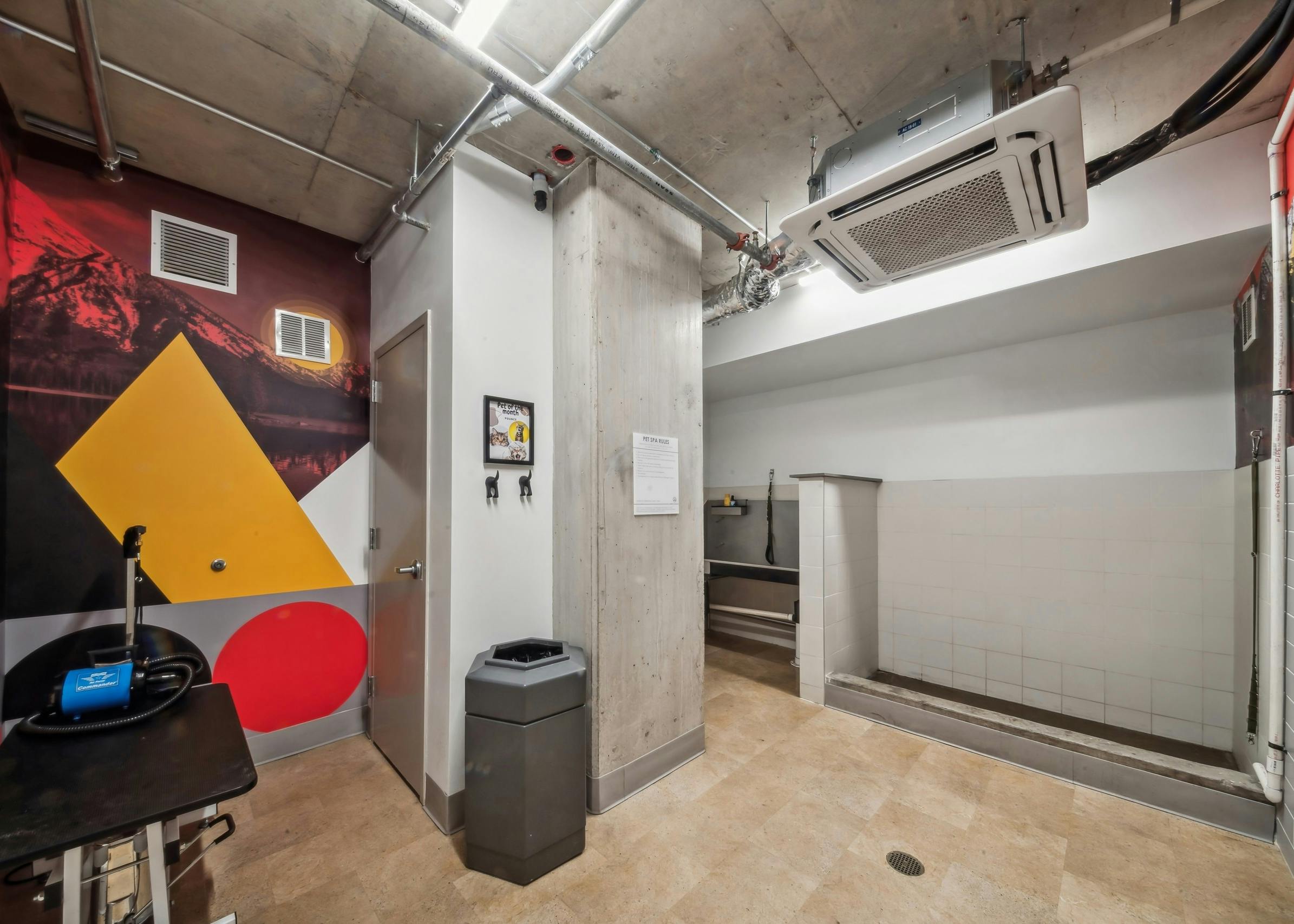 A paw wash at AMLI Broadway Park featuring a grooming table, a trash can and a white tiled area and a sink in back of room.