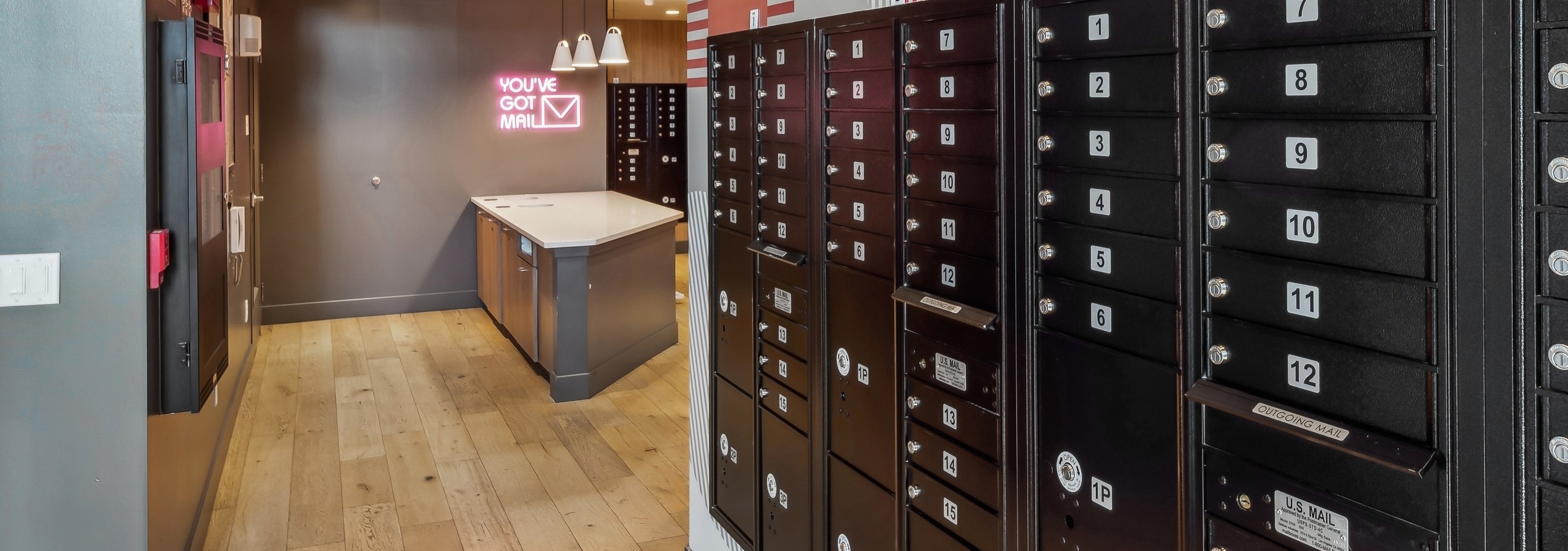 Black numbered mailboxes at AMLI Broadway Park and a neon sign reading "You've Got Mail" above small countertop space in back of mailroom