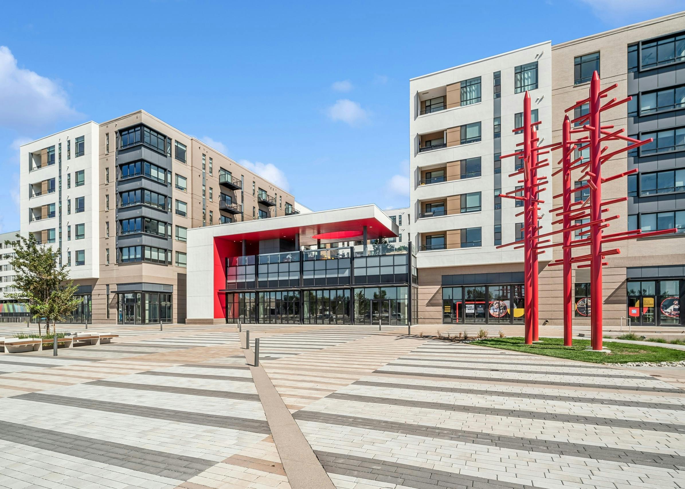 The modern white and tan AMLI Broadway Park apartment building with red architectural accents and red metal sculpture at Byers Square