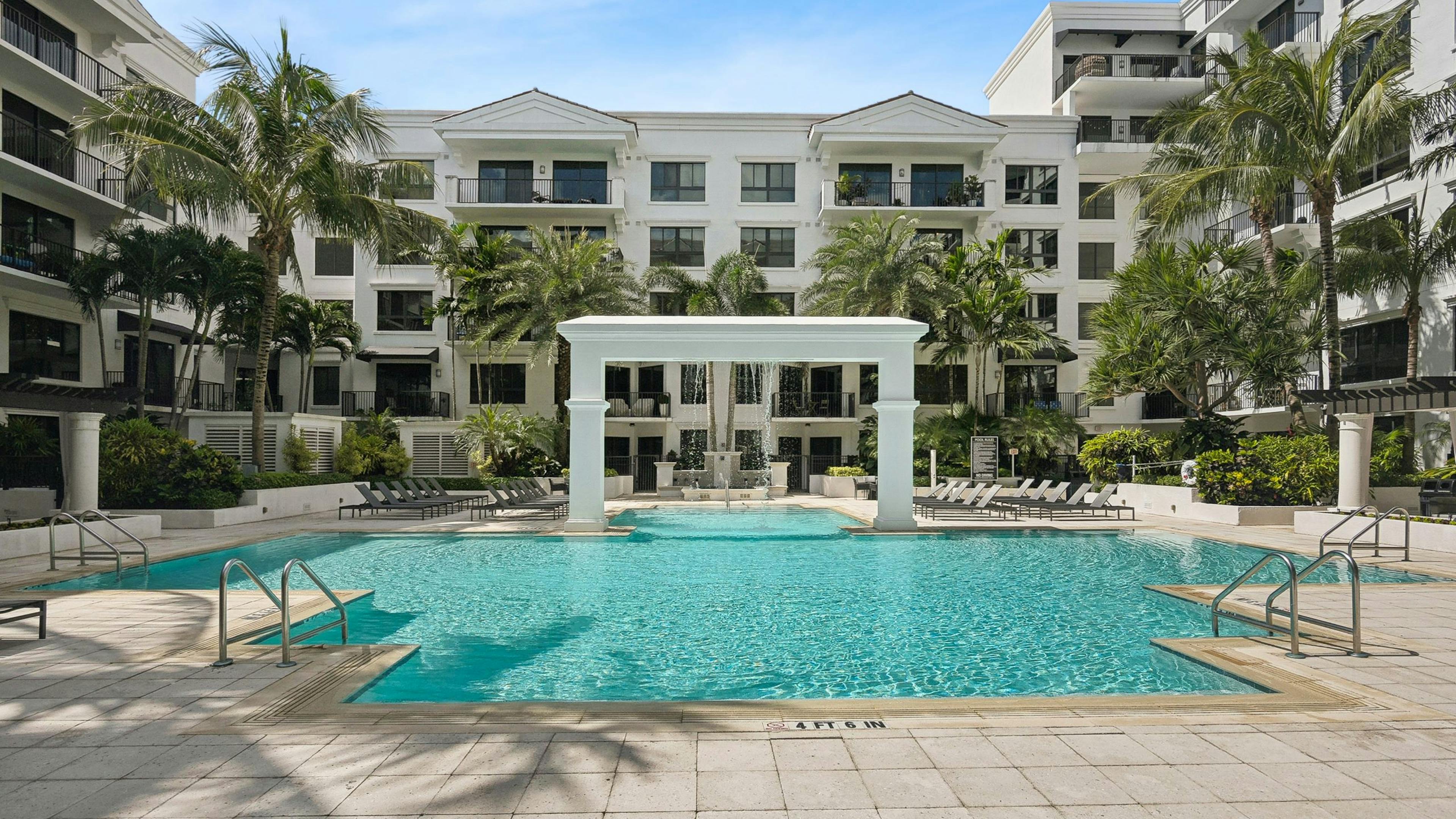 Luxurious outdoor swimming pool area at AMLI Joya with a central arch structure and lounge chairs and palm trees surrounding it