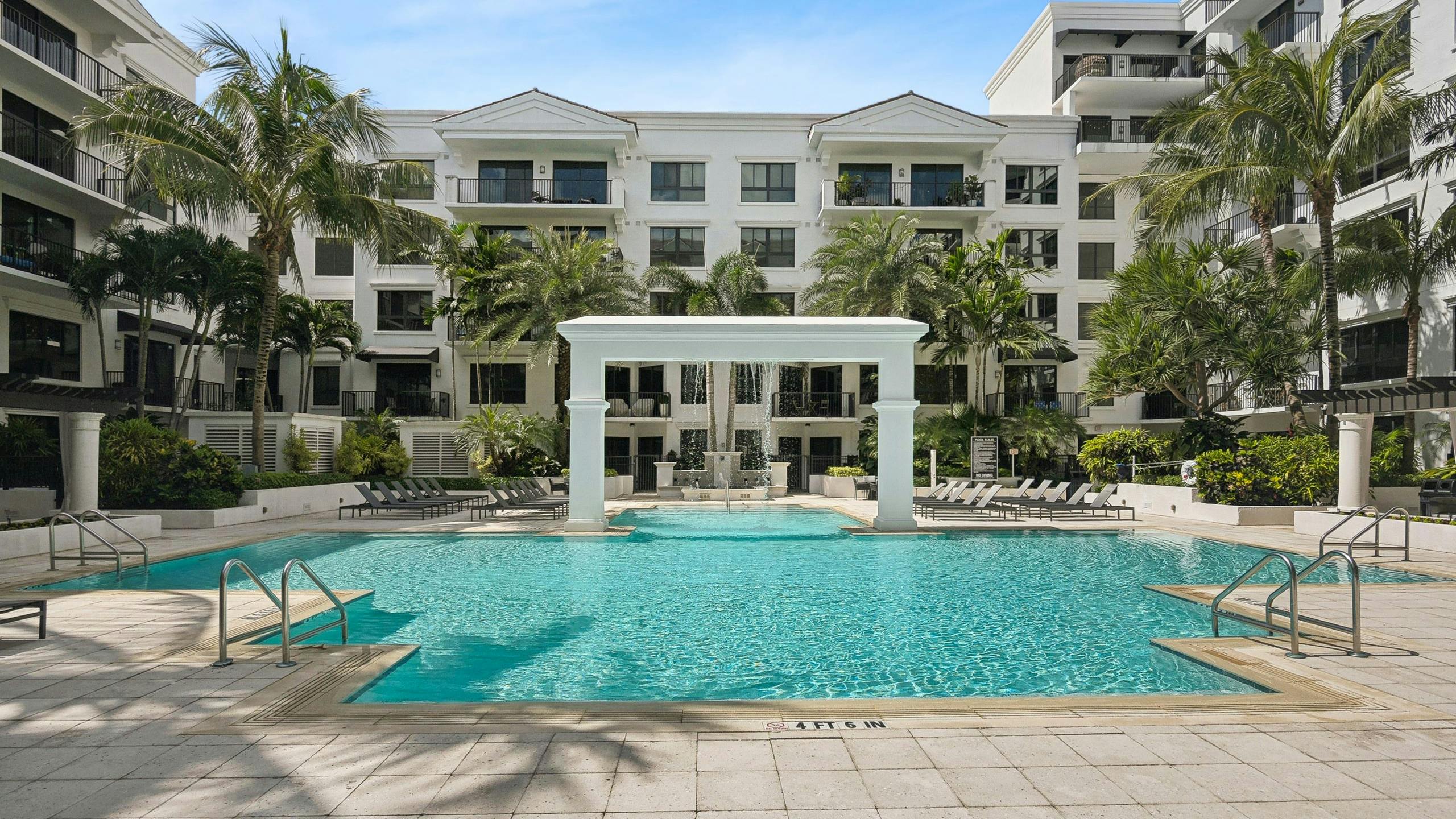 Luxurious outdoor swimming pool area at AMLI Joya with a central arch structure and lounge chairs and palm trees surrounding it