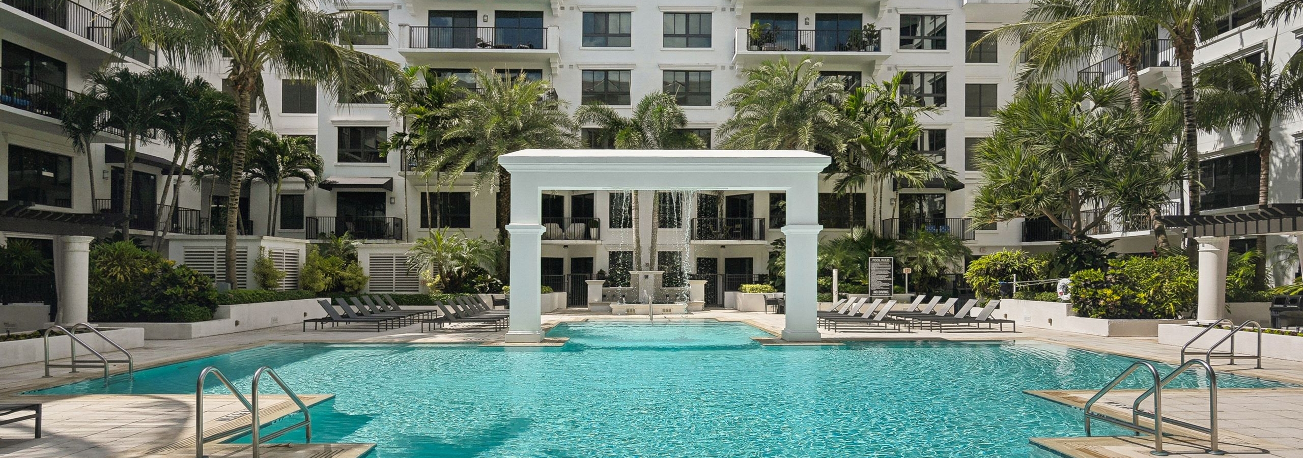 Luxurious outdoor swimming pool area at AMLI Joya with a central arch structure and lounge chairs and palm trees surrounding it