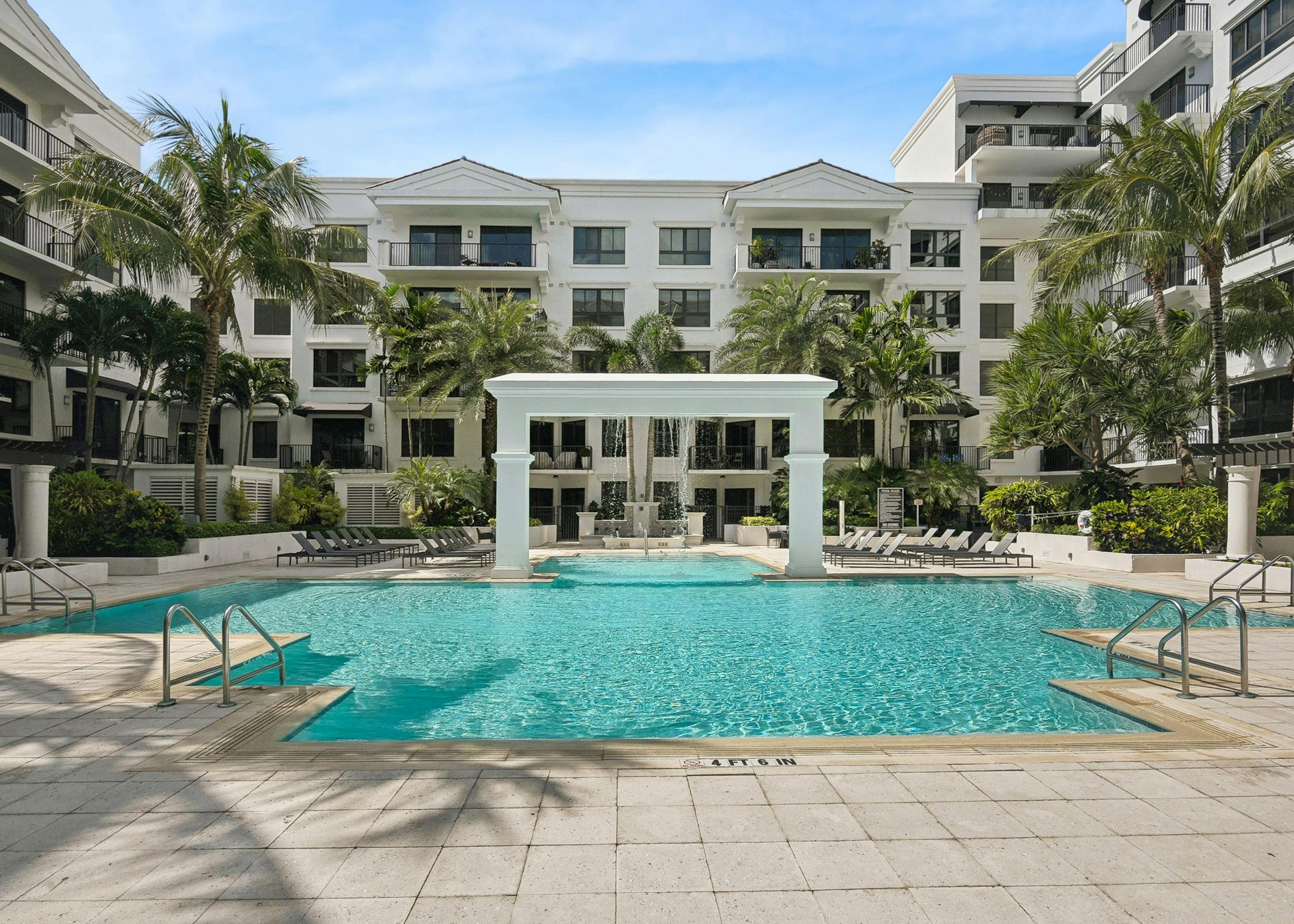 Luxurious outdoor swimming pool area at AMLI Joya with a central arch structure and lounge chairs and palm trees surrounding it
