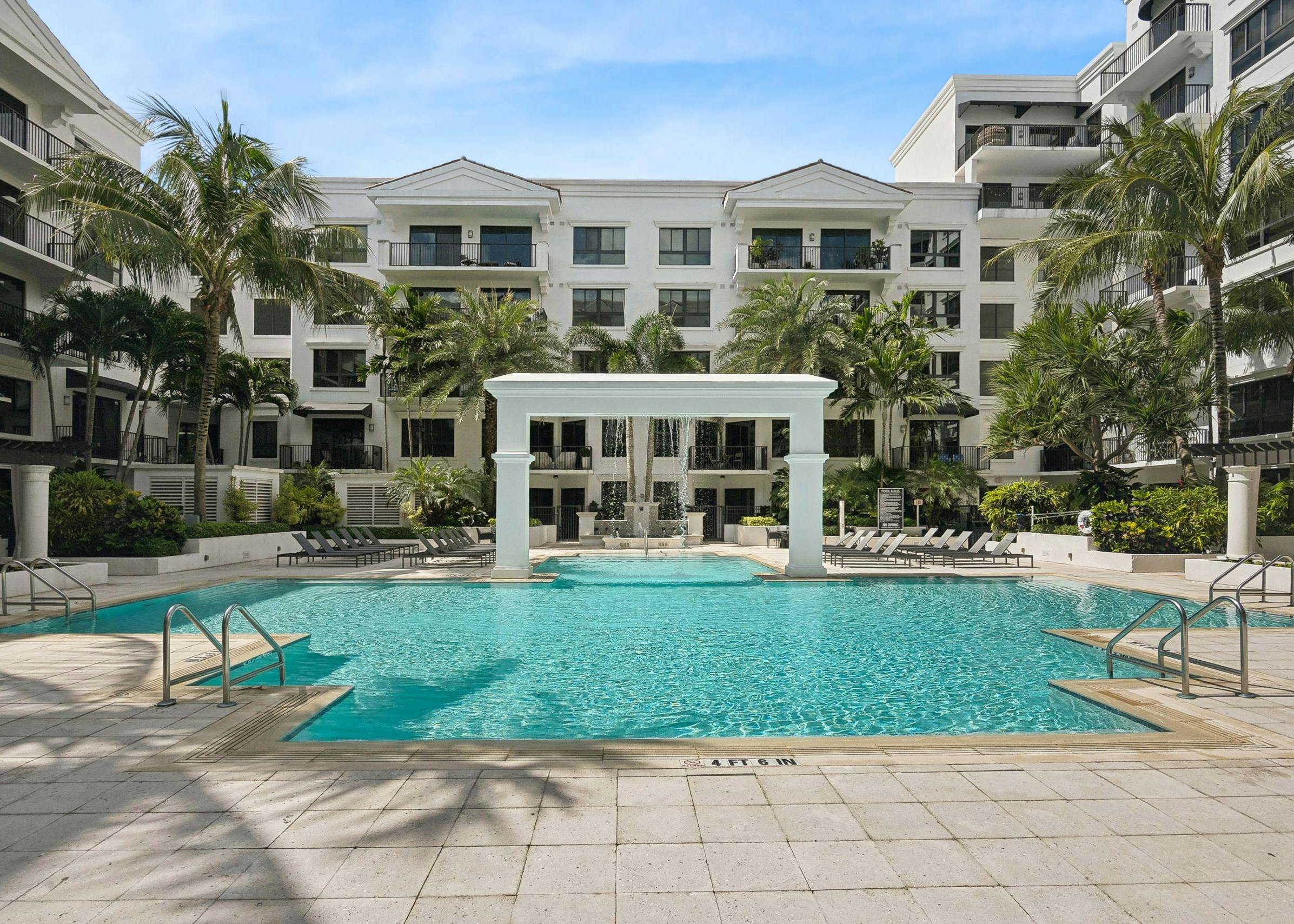 Luxurious outdoor swimming pool area at AMLI Joya with a central arch structure and lounge chairs and palm trees surrounding it