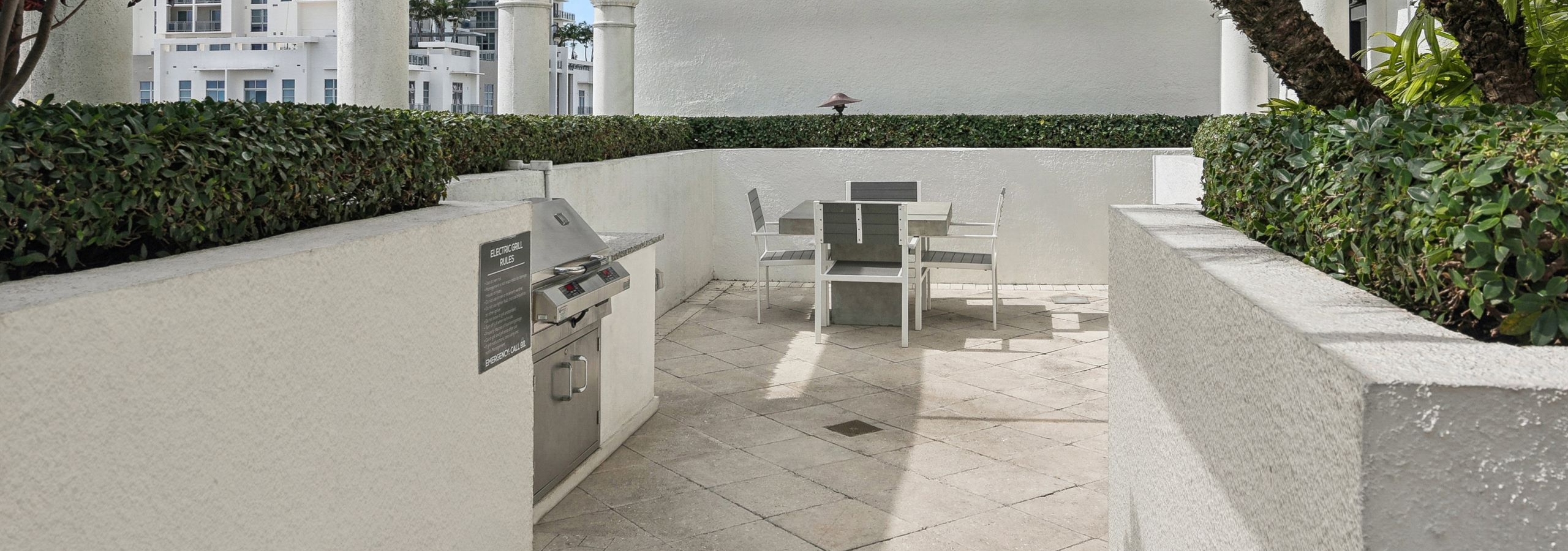AMLI Joya apartments rooftop with a built in stainless steel grill and table with four chairs and lush greenery along the walls