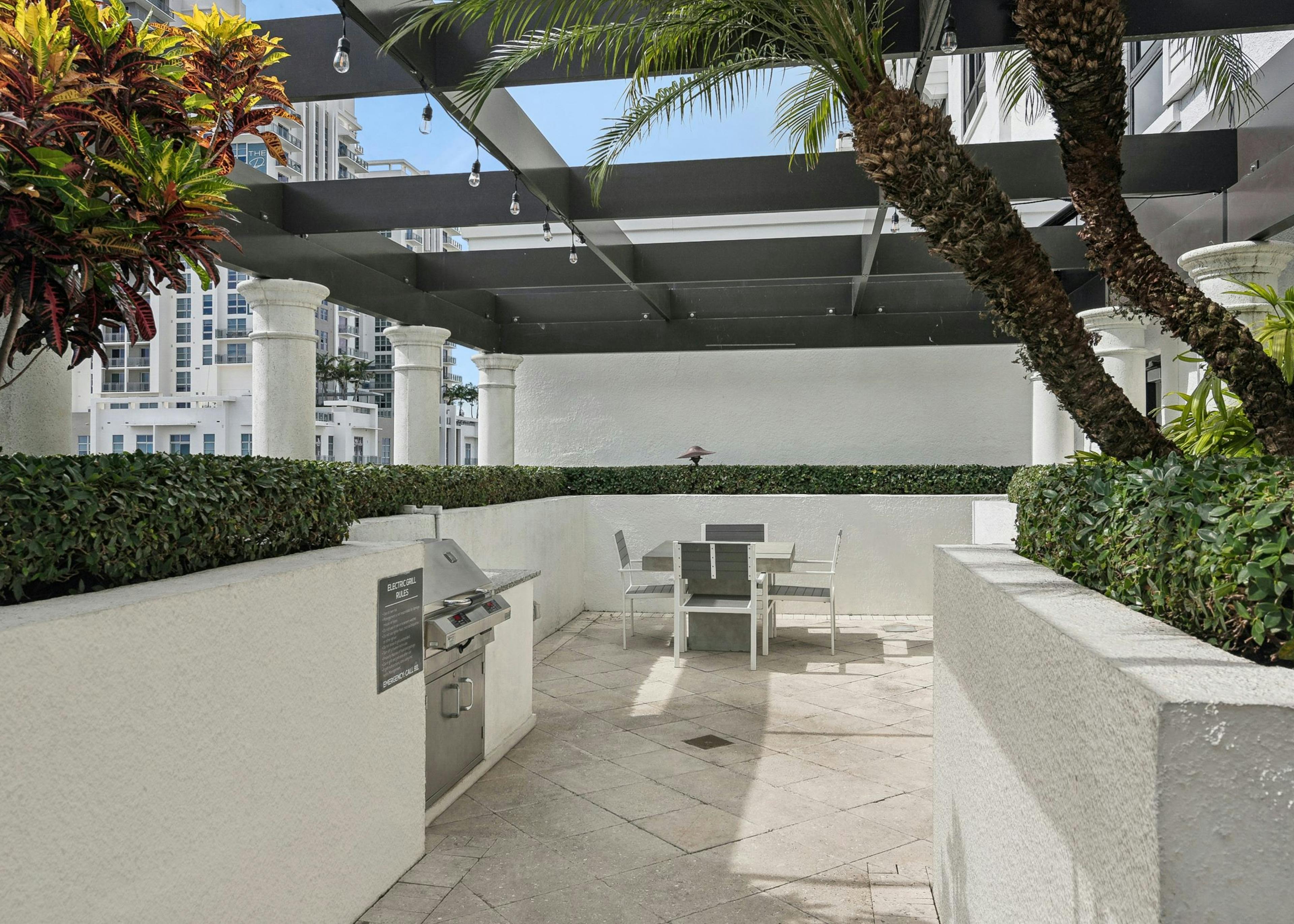 AMLI Joya apartments rooftop with a built in stainless steel grill and table with four chairs and lush greenery along the walls