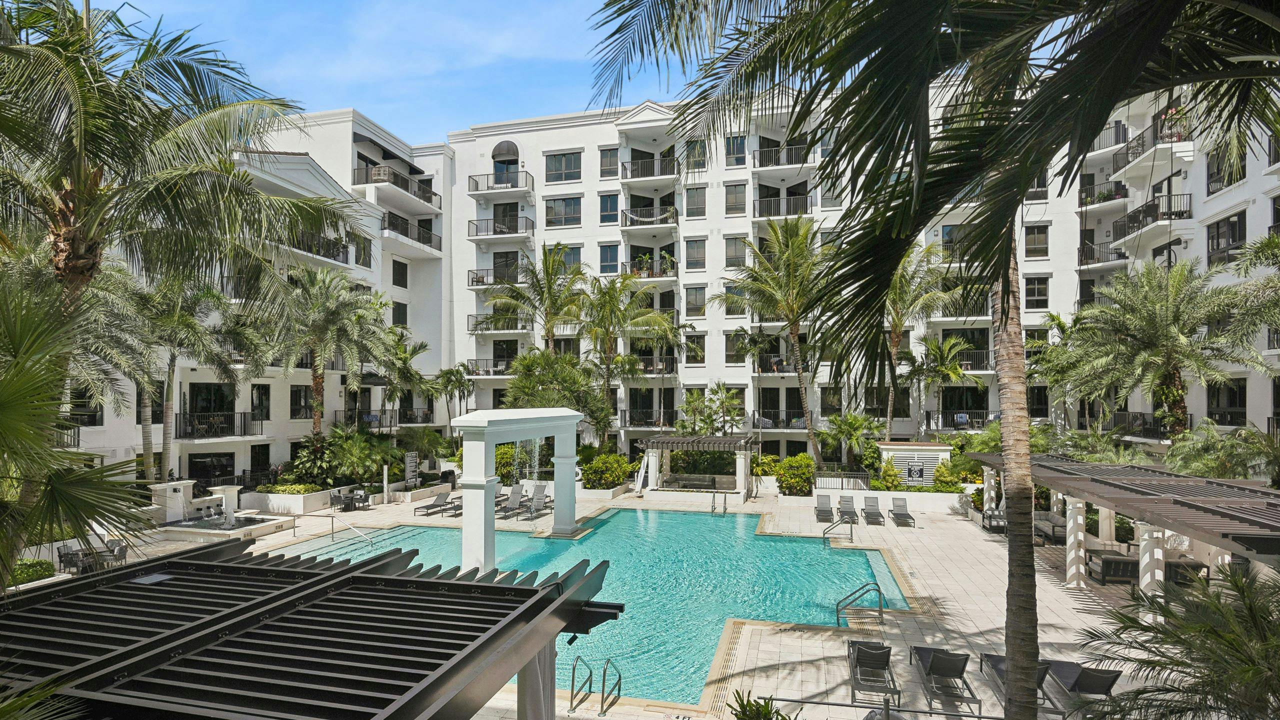 Aerial view of AMLI Joya apartments resort style pool featuring a central arch with a brown pergola, lounging chairs and palm trees