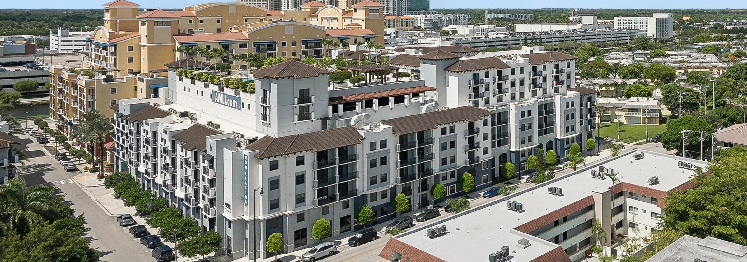 Aerial view of AMLI Dadeland apartment building with brown and white exterior surrounded by smaller buildings and trees in an urban area