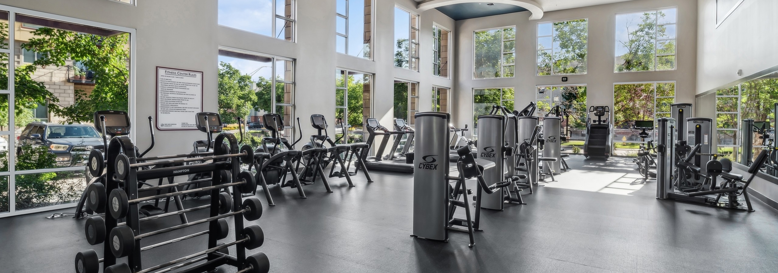 A fitness center at AMLI Cherry Creek apartments with strength training machines, weights, elliptical machines and floor to ceiling windows.