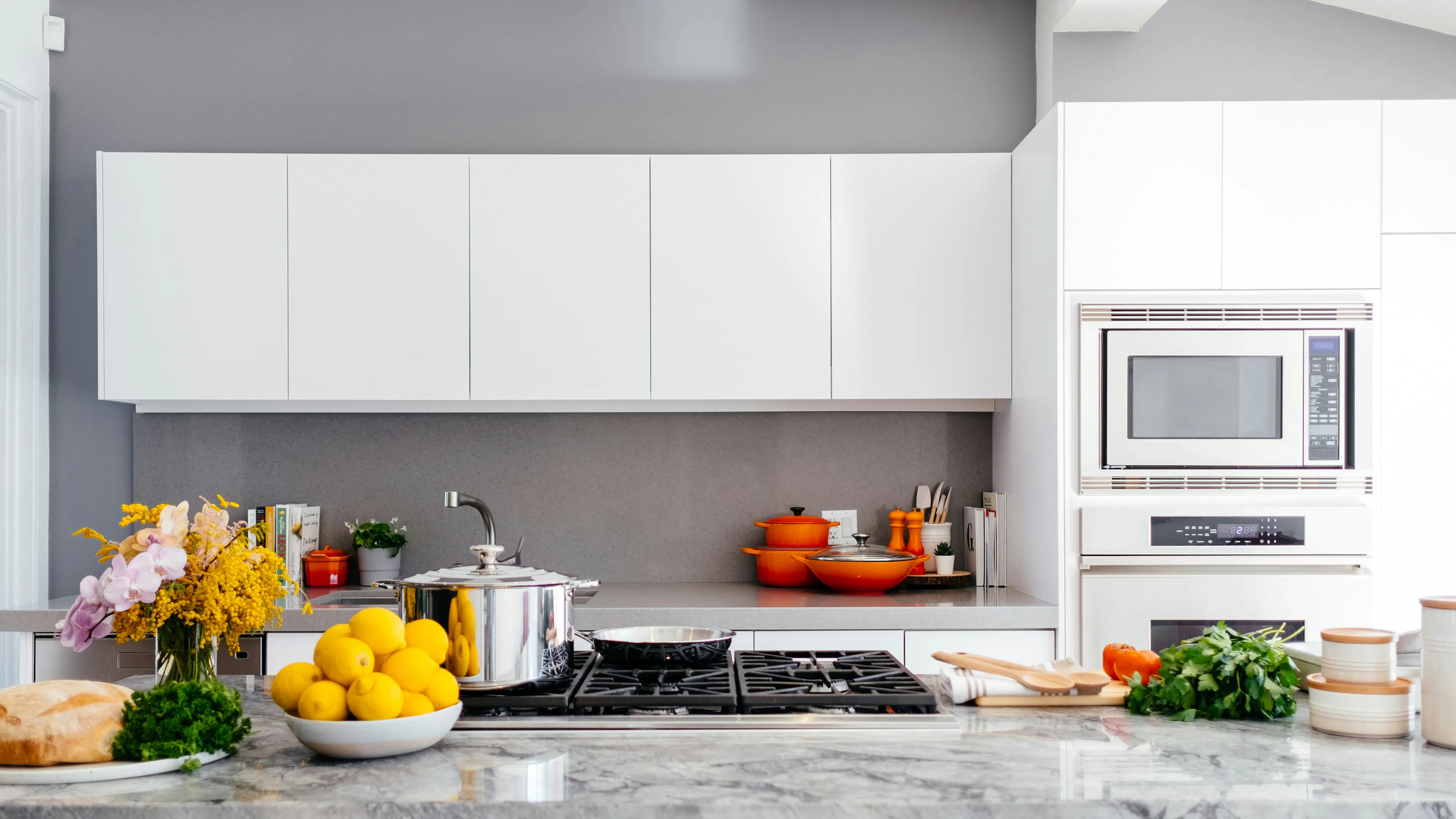 A white and marble apartment kitchen with several bowls on the counter filled with colorful fruits