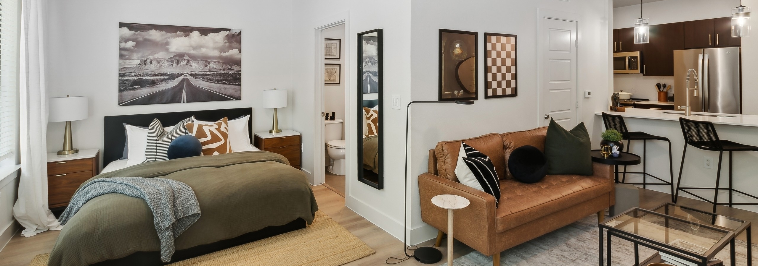 AMLI at the Ballpark studio apartment featuring a bed and living area with a brown leather couch and kitchen with stainless appliances