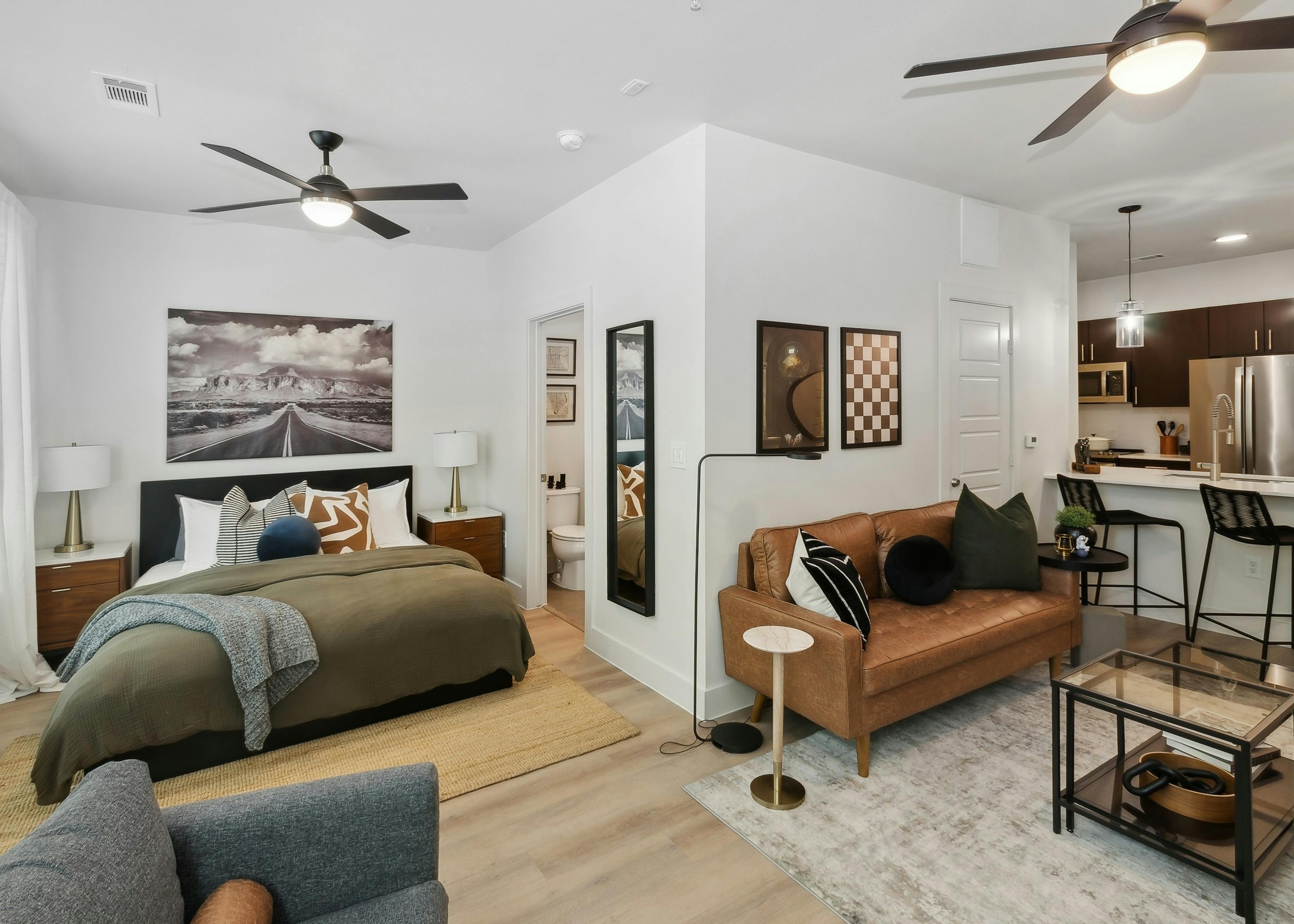 AMLI at the Ballpark studio apartment featuring a bed and living area with a brown leather couch and kitchen with stainless appliances